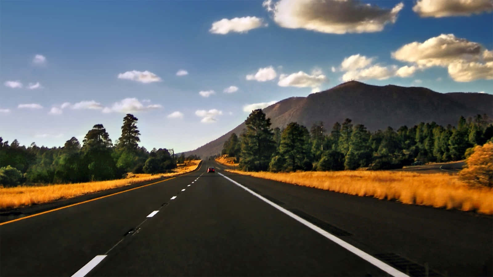 highway 桌布 壁紙 — 一輛孤獨的紅色汽車在一條筆直的瀝青路上行駛，兩旁是金色的草地和綠樹，頭頂是明亮的藍天和蓬鬆的白雲。