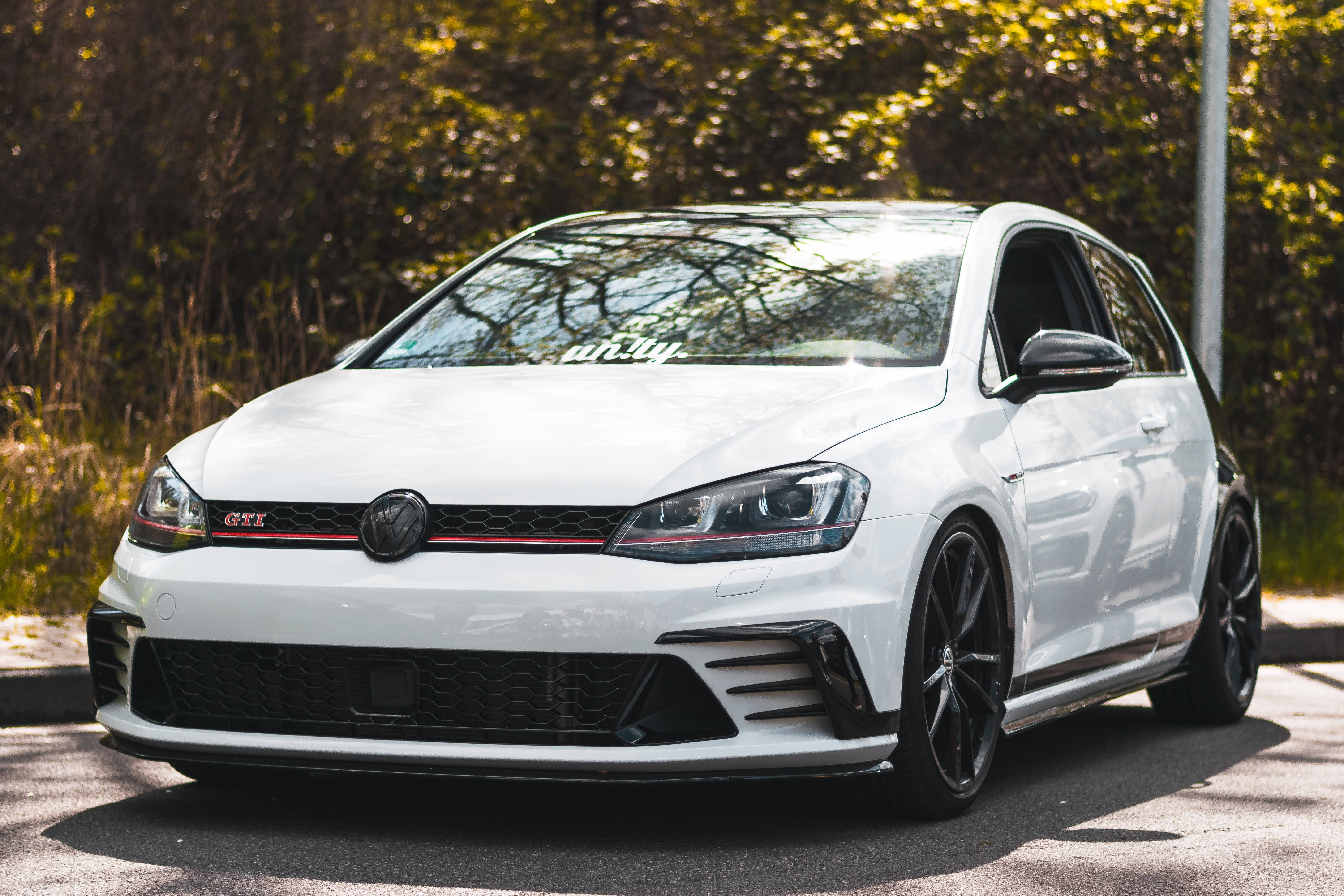 福斯汽車 桌布 壁紙 — 一輛完美無瑕的白色 Volkswagen Golf GTI 停在柏油路上，背景是陽光普照的樹木。