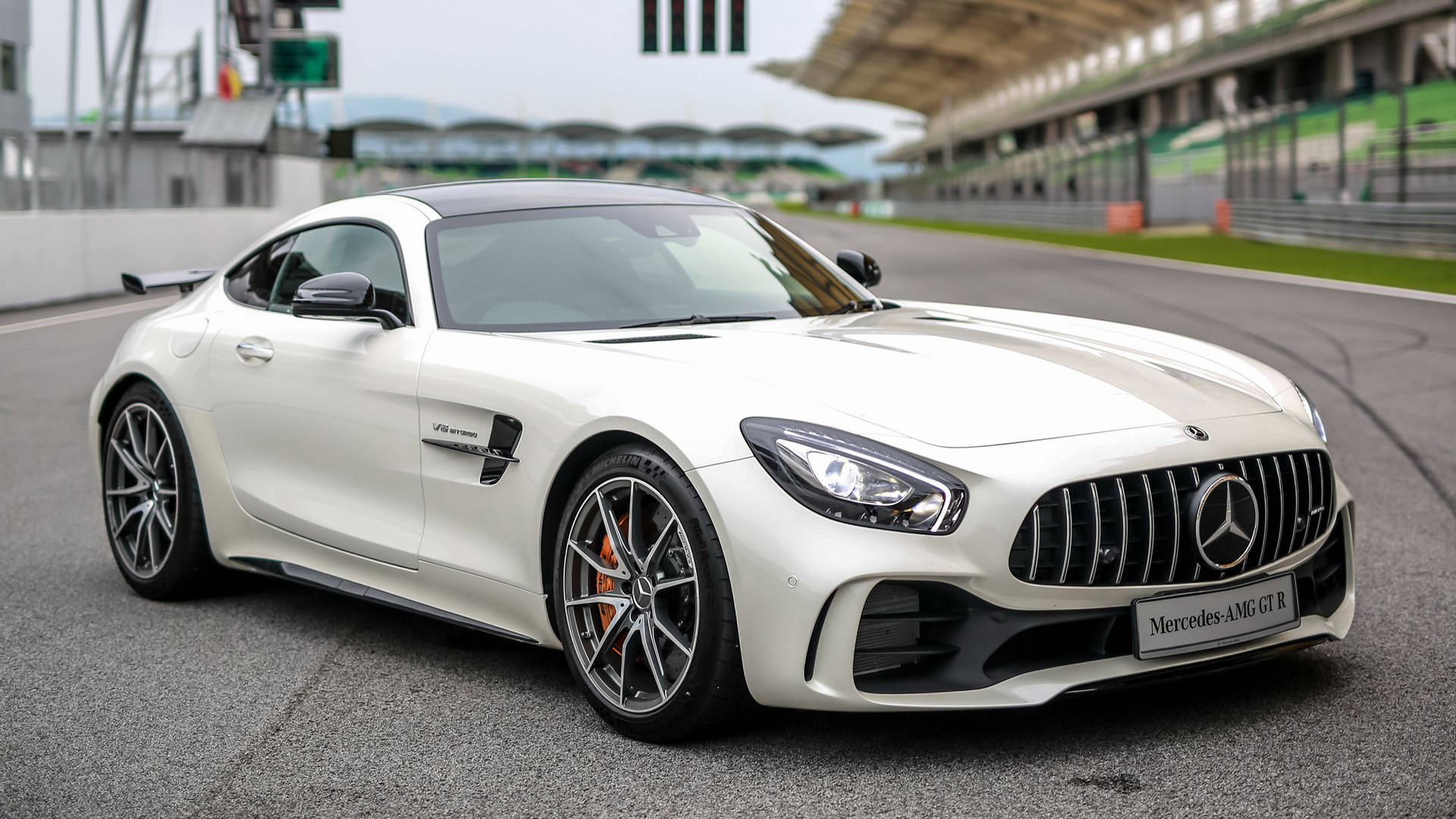 Gtr 桌布 壁紙 — 一輛完美無瑕的白色Mercedes-AMG GT R跑車停在賽道上，背景是觀眾席和遠山，呈現柔和焦點。