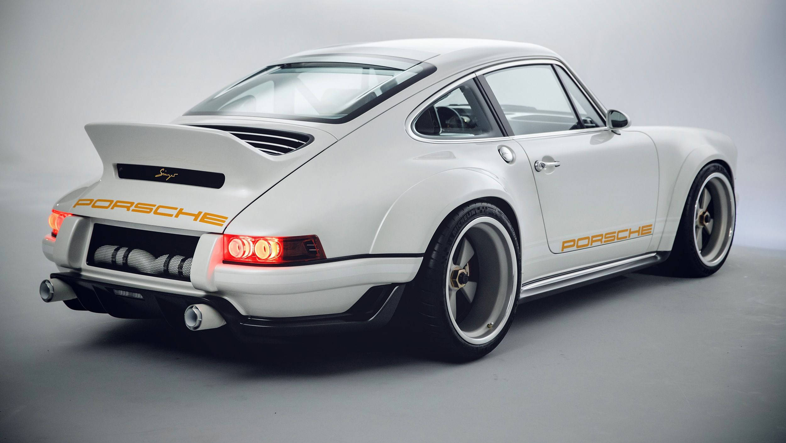 Singer 桌布 壁紙 — 一輛完美無瑕的白色保時捷911經典跑車，帶有金色點綴和發光的紅色尾燈，以極簡灰色工作室背景為襯托。