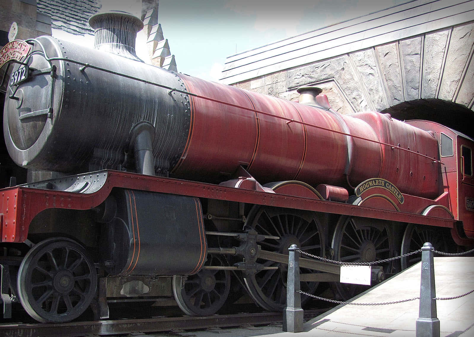 Hogwarts Express 桌布 壁紙 — 一輛宏偉的紅色霍格華茲特快蒸汽火車頭在石拱門下展出，設有鏈條屏障。