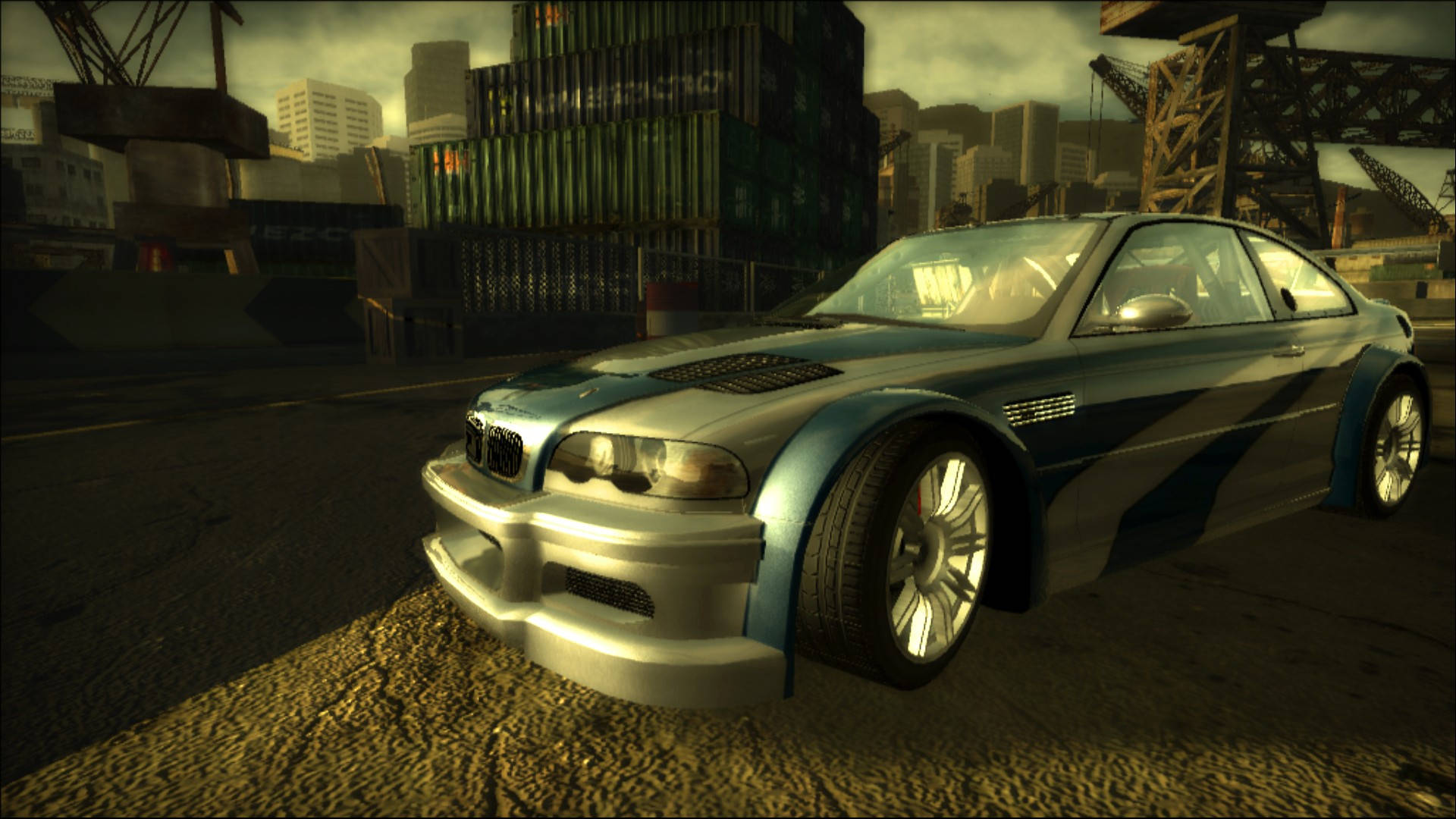 Need For Speed 桌布 壁紙 — 一輛定製的銀色和藍色BMW M3跑車停泊在一個佈滿貨櫃和起重機的粗糙城市碼頭，背景是朦朧的日落天空。