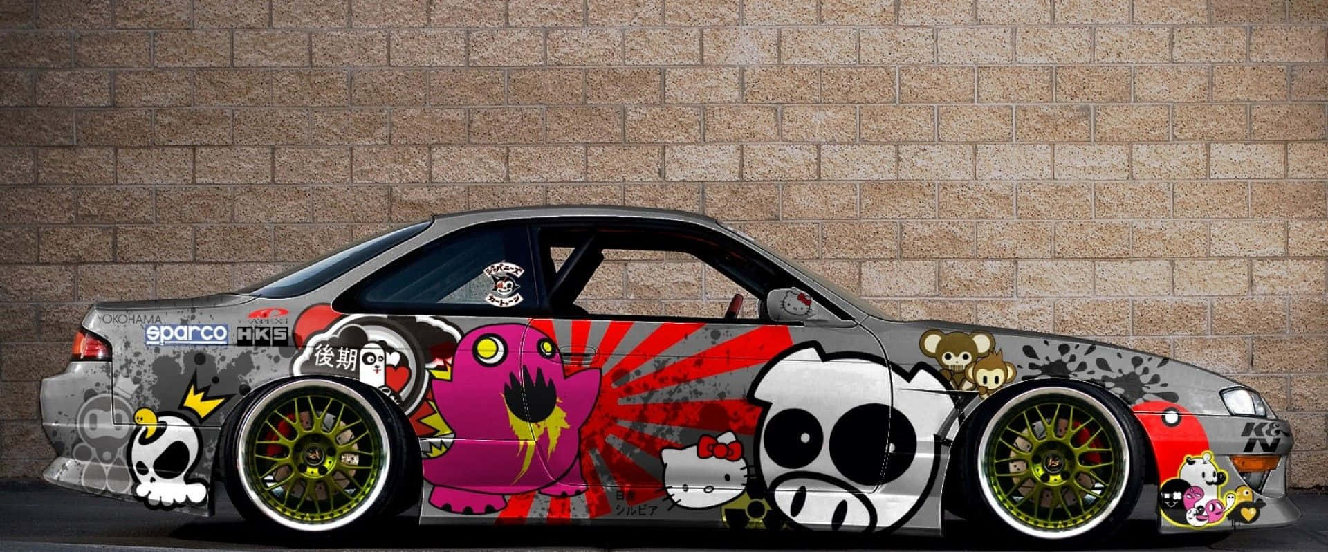 JDM汽車 桌布 壁紙 — 一輛客製化的塗鴉覆蓋的飄移車，帶有卡通角色和紅色潑濺藝術，停靠在磚牆前。