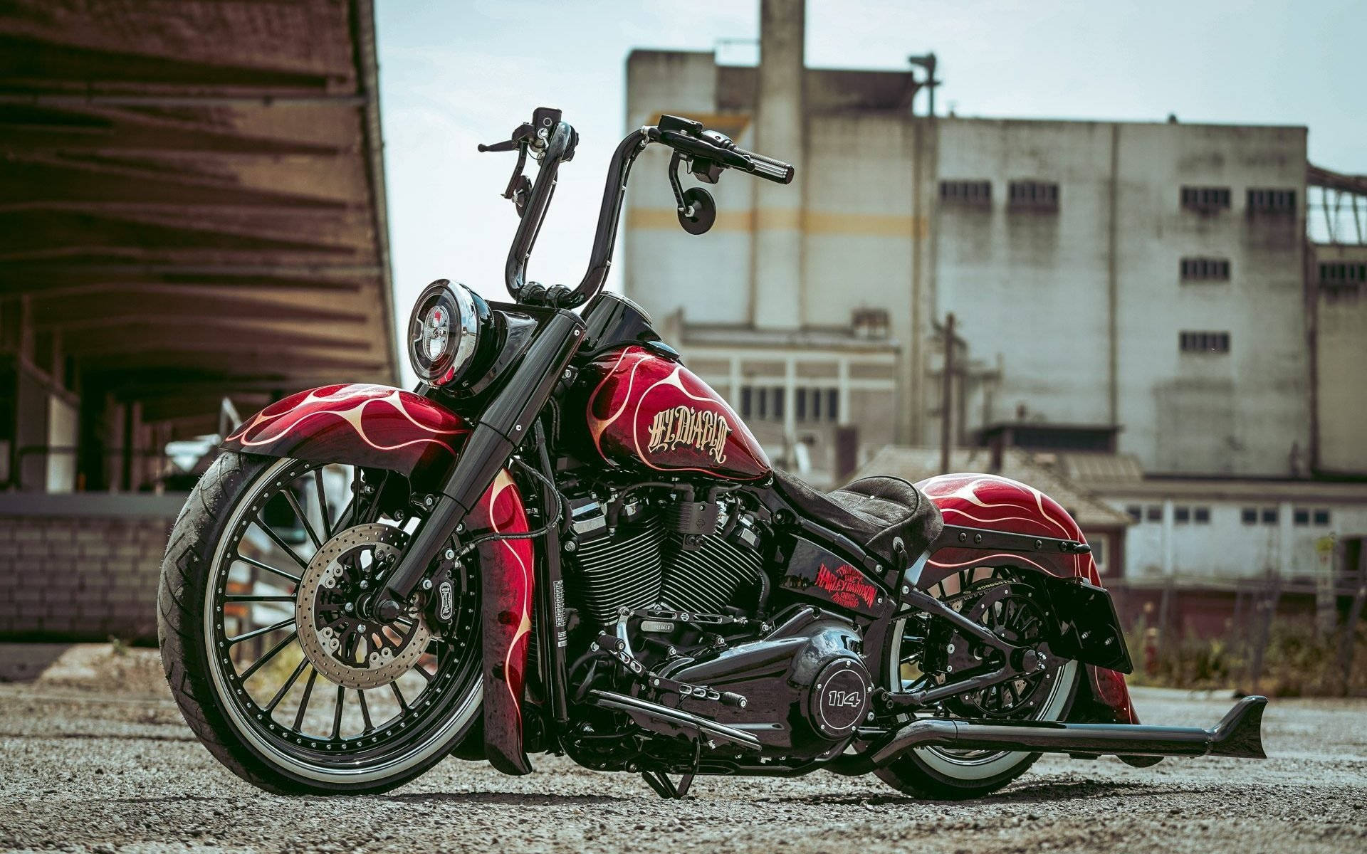 Harley 桌布 壁紙 — 一輛客製化紅色火焰塗裝哈雷戴維森機車停放在工業建築前的礫石上。