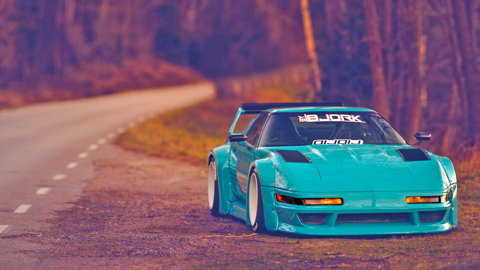 corvette 桌布 壁紙 — 一輛帶有 'BJORK' 貼紙的鮮豔青綠色甩尾車，在黃金時刻停泊在蜿蜒的林間道路上。