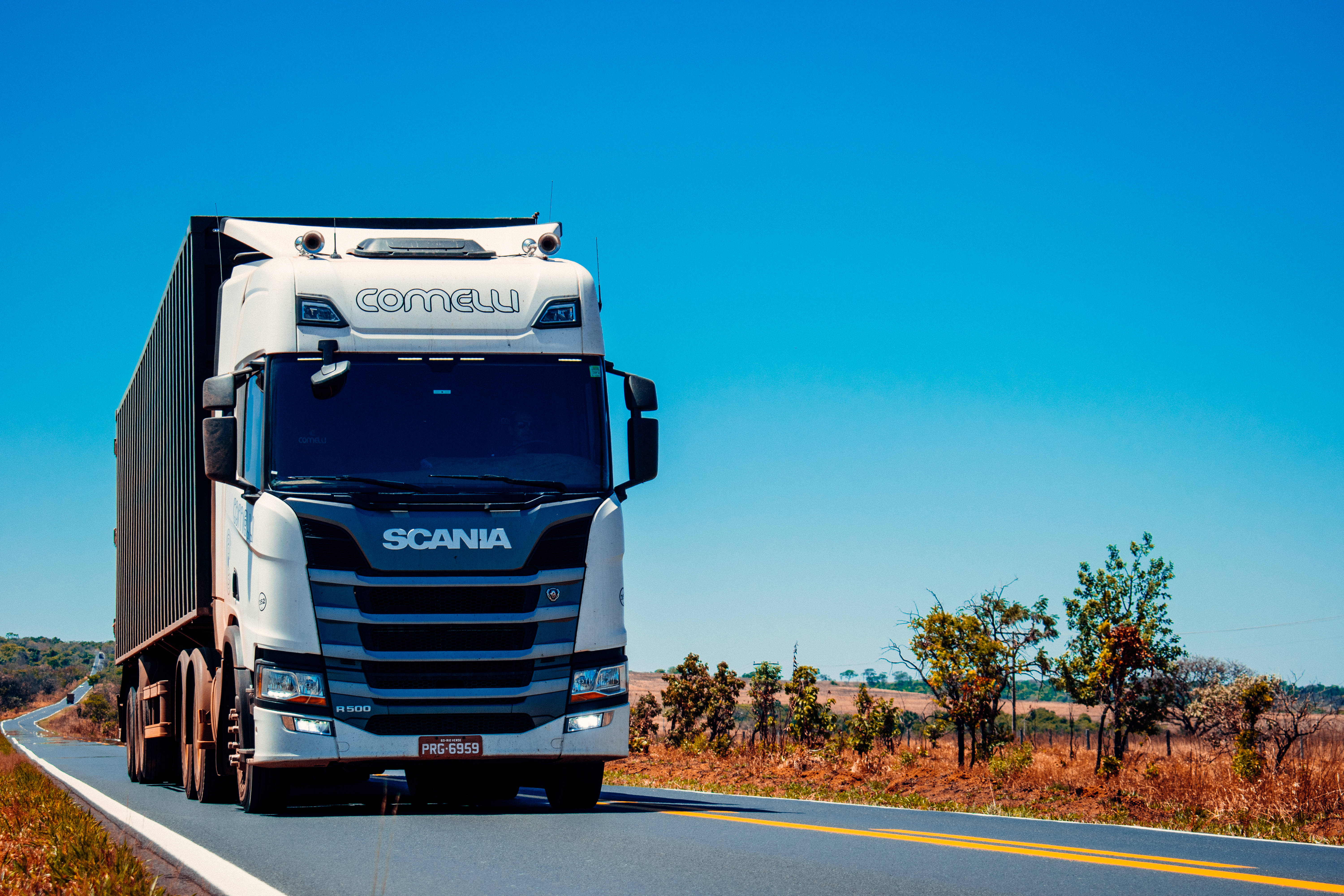Truck 桌布 壁紙 — 一輛帶有 'Cornelli' 標誌的白色 Scania 卡車在晴朗藍天下，行駛在陽光普照的高速公路上，穿過乾燥的草原。