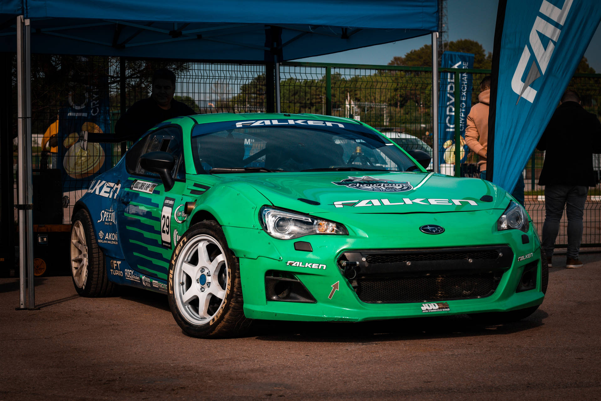 帶有 Falken 標誌的綠色賽車停在賽事藍色帳篷下。 — 4K 壁紙