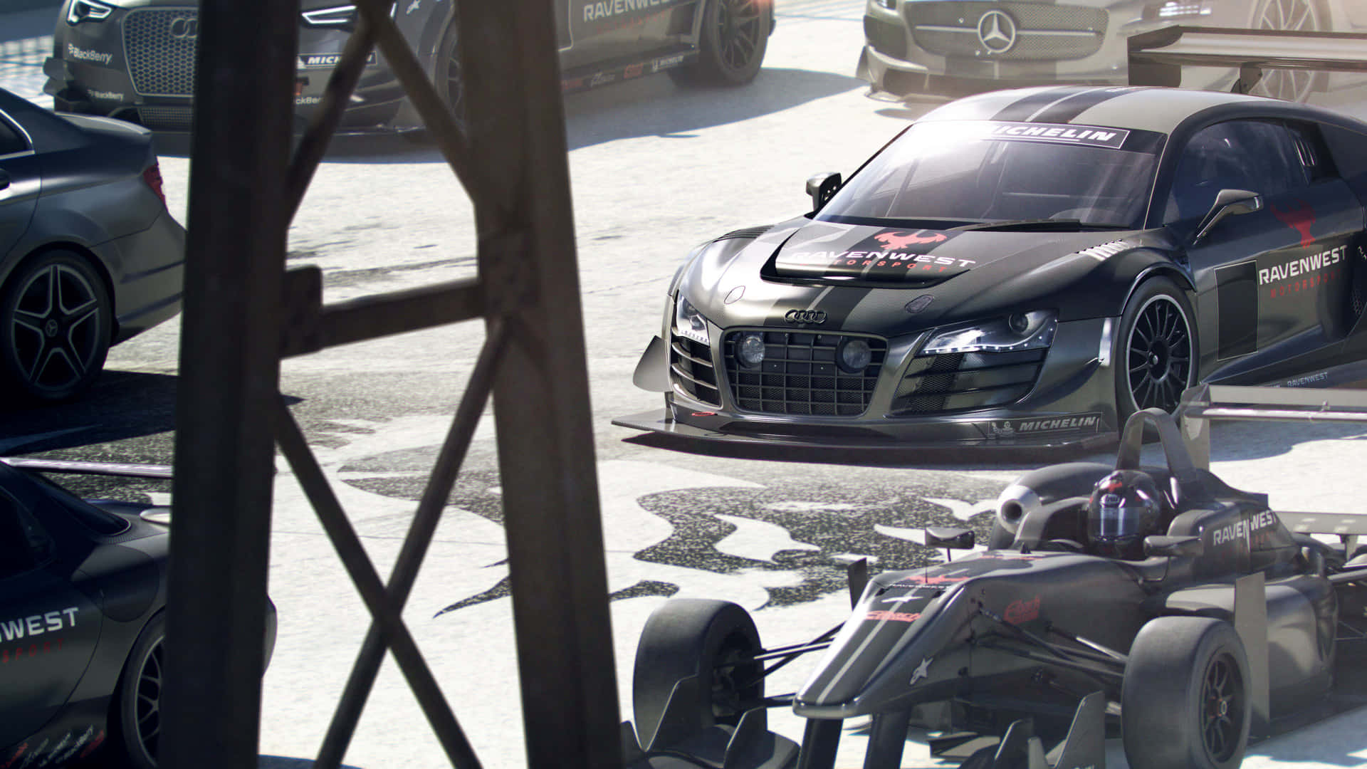 iPhone X Grid Autosport 桌布 壁紙 — 一輛帶有 'RavenWest' 品牌的時尚黑色奧迪 R8 賽車在明亮的日光下停在維修站車庫內，旁邊是一輛一級方程式賽車。