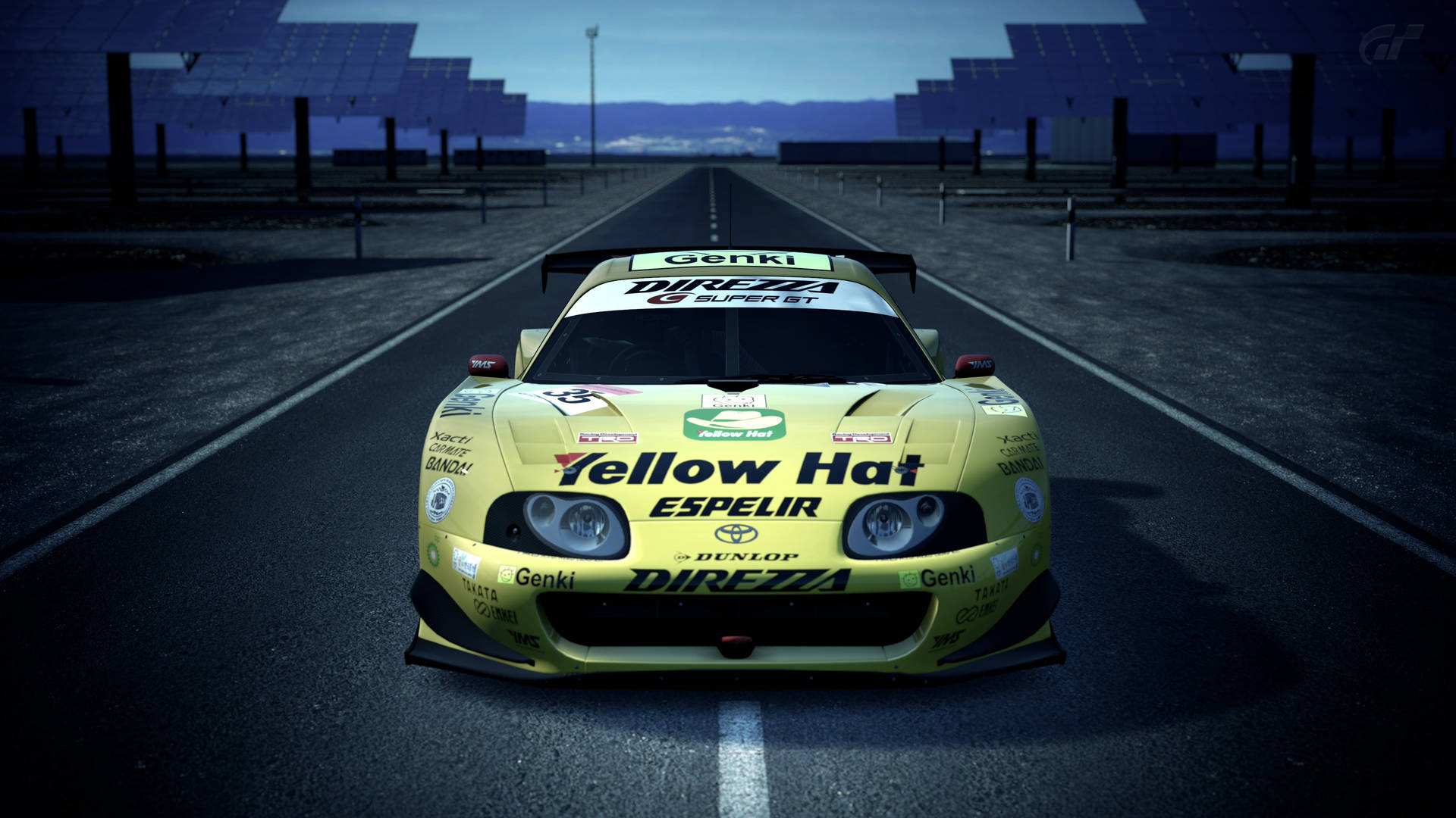黃昏時分，黃色賽車在黑暗的賽道上，背景有太陽能板。 — Toyota Supra Mk4 壁紙