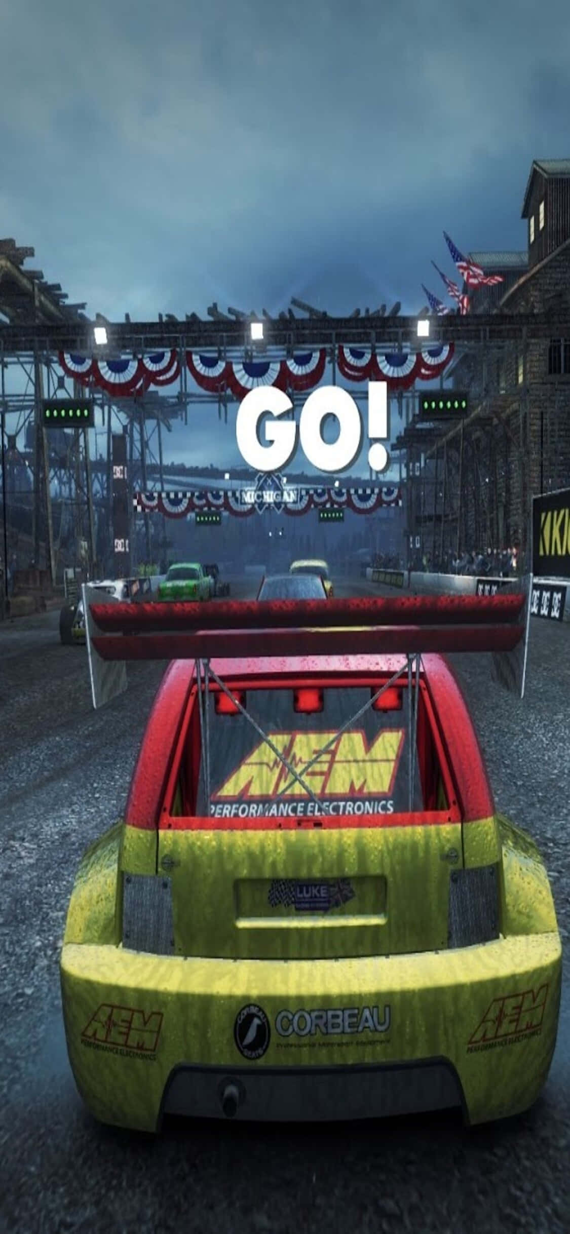 iPhone Xs Dirt Showdown 桌布 壁紙 — 一輛帶有AEM貼紙的鮮豔黃紅賽車，在黃昏時分於「GO！」標誌下，在濕滑的城市賽道上飛馳。
