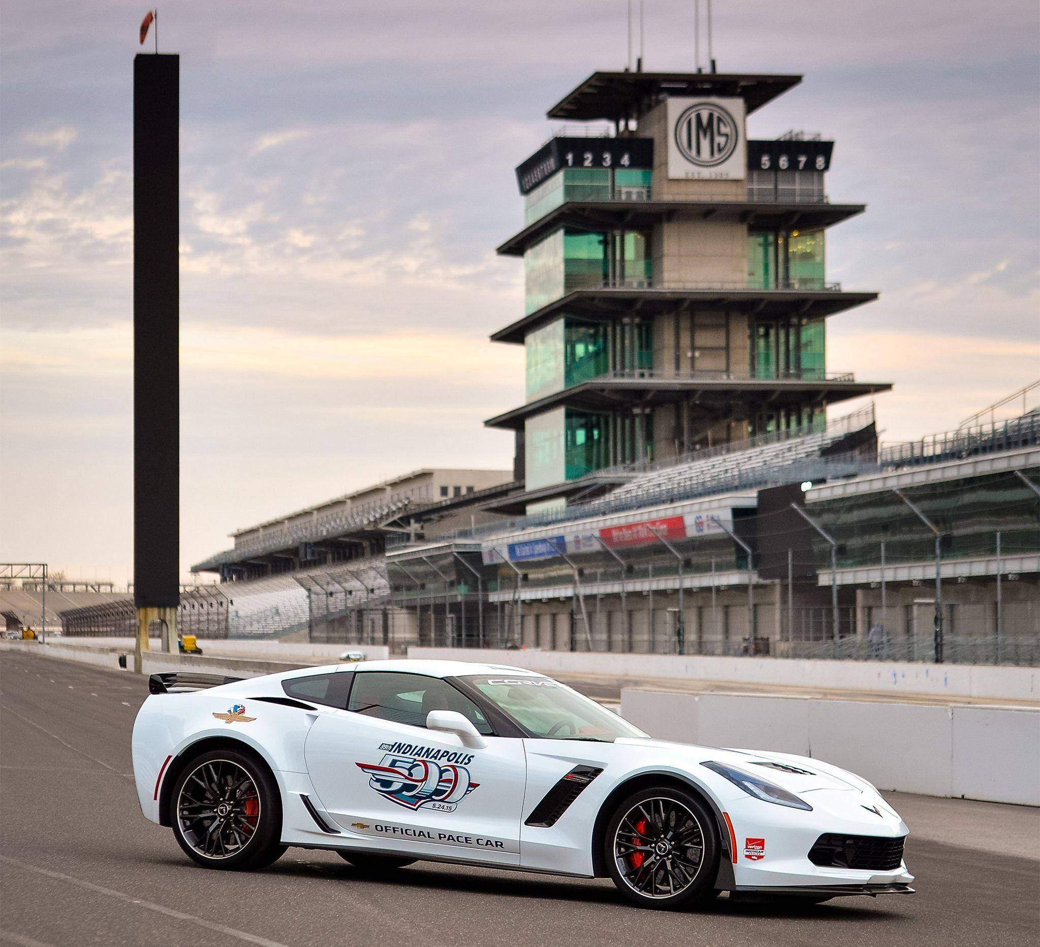 Indianapolis 桌布 壁紙 — 一輛帶有Indy 500貼紙的白色Corvette Pace Car停在空蕩蕩的賽道上，背景是陰天和標誌性的IMS塔。