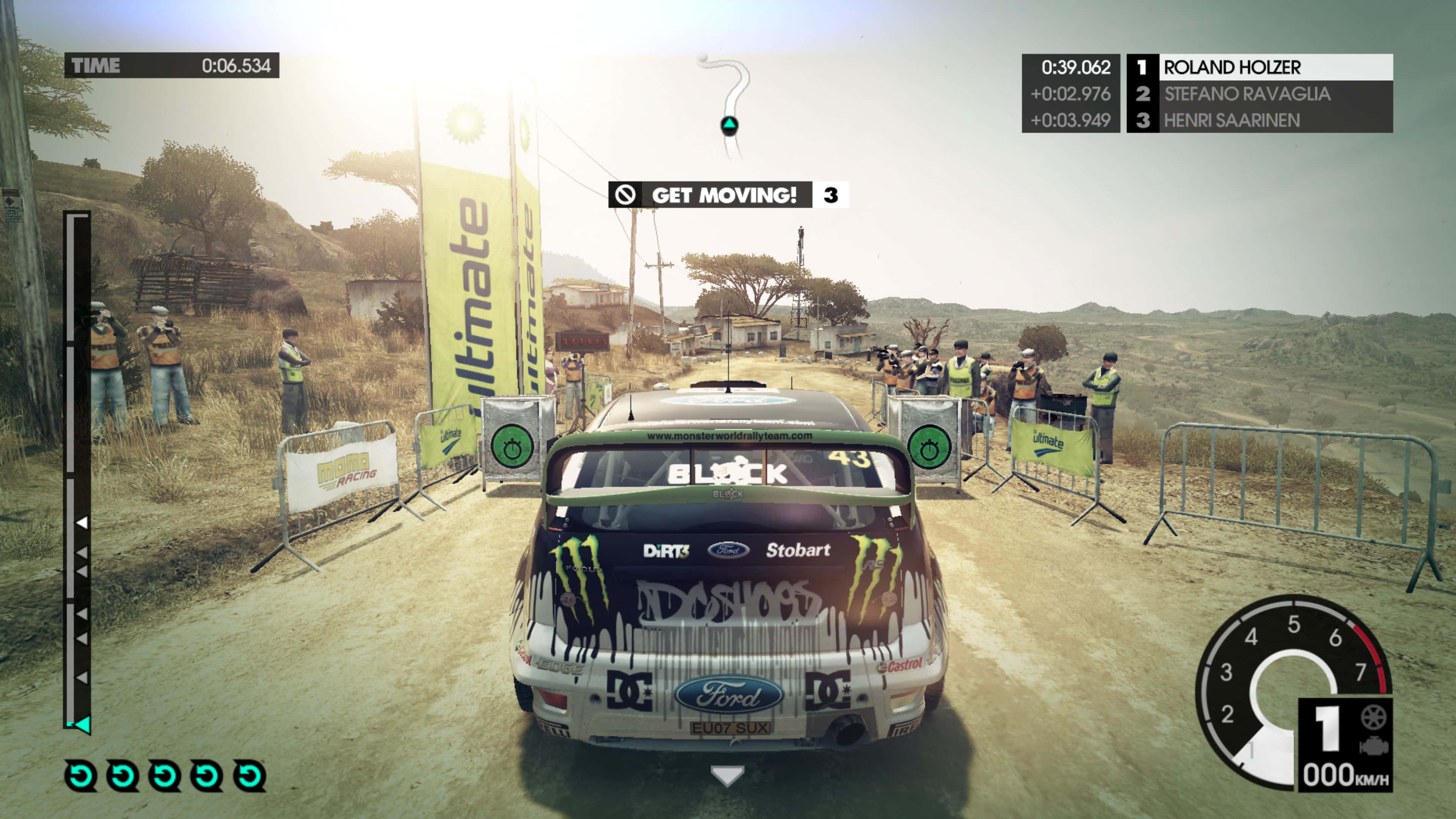 4K Dirt 3 桌布 壁紙 — 一輛帶有Monster Energy貼紙的福特拉力賽車，在明亮的日光下，沿著一條塵土飛揚、兩旁有觀眾和護欄的鄉村道路飛馳。