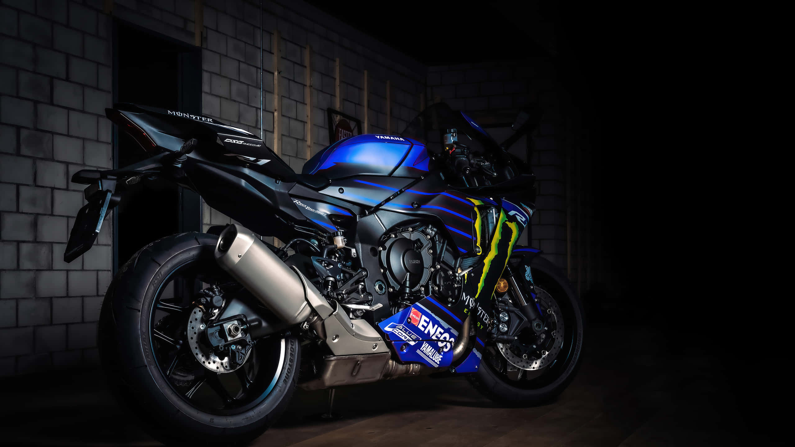 桌布 壁紙 — 一輛帶有Monster Energy品牌標誌的時尚藍黑Yamaha R1機車，在黑暗的磚牆車庫中被戲劇性地照亮。