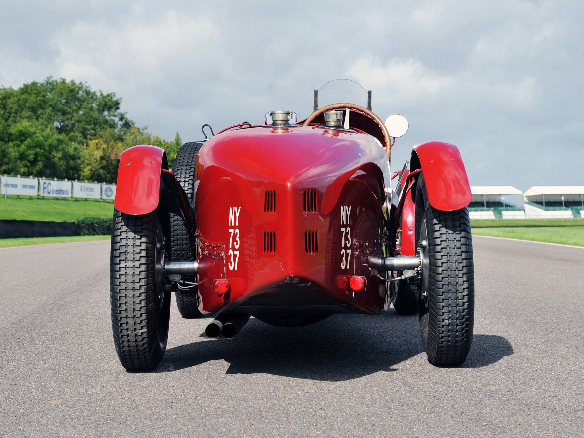 bugatti iPhone 桌布 壁紙 — 一輛帶有NY 73 37標記的光澤紅色復古賽車，在陰天停泊在瀝青賽道上。