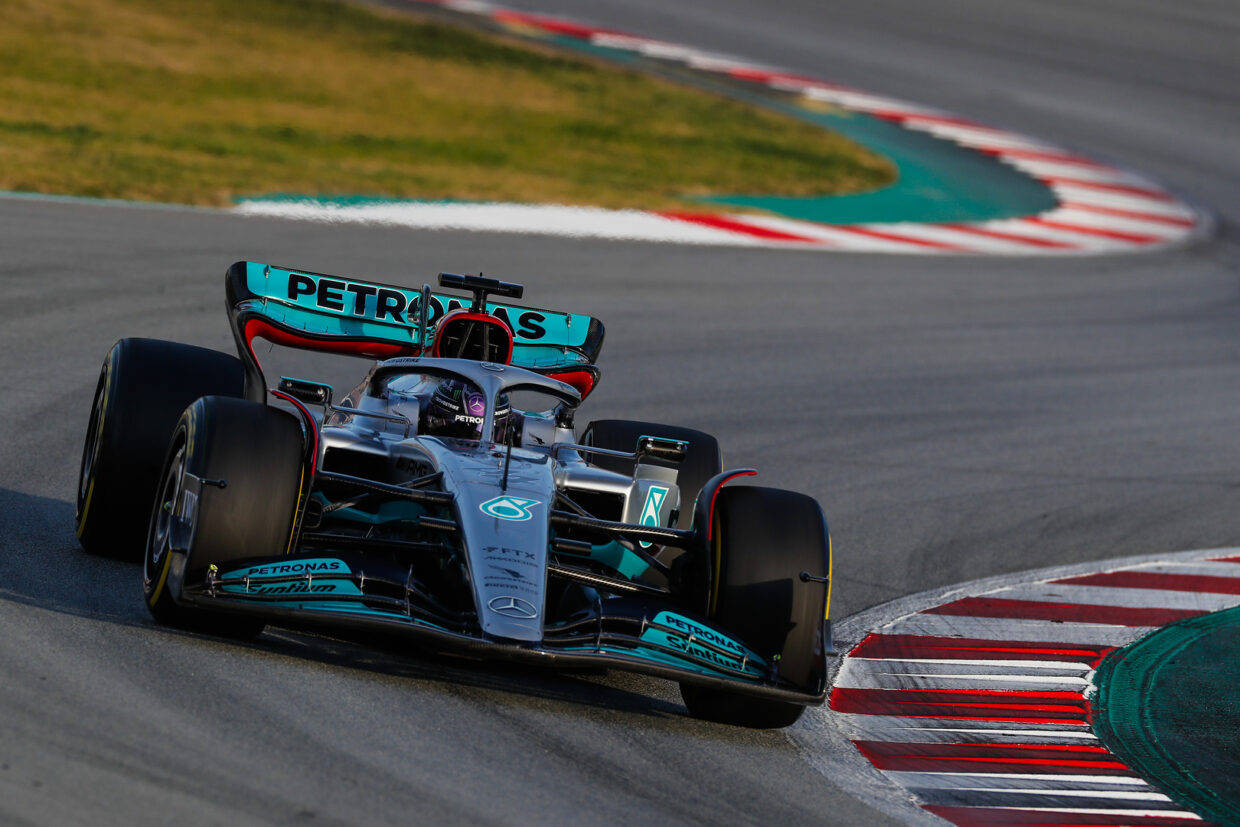 Mercedes 桌布 壁紙 — 一輛帶有Petronas塗裝的Mercedes F1賽車在陽光明媚的賽道上疾馳過一個急彎，賽道邊緣有紅、白、綠三色路肩。