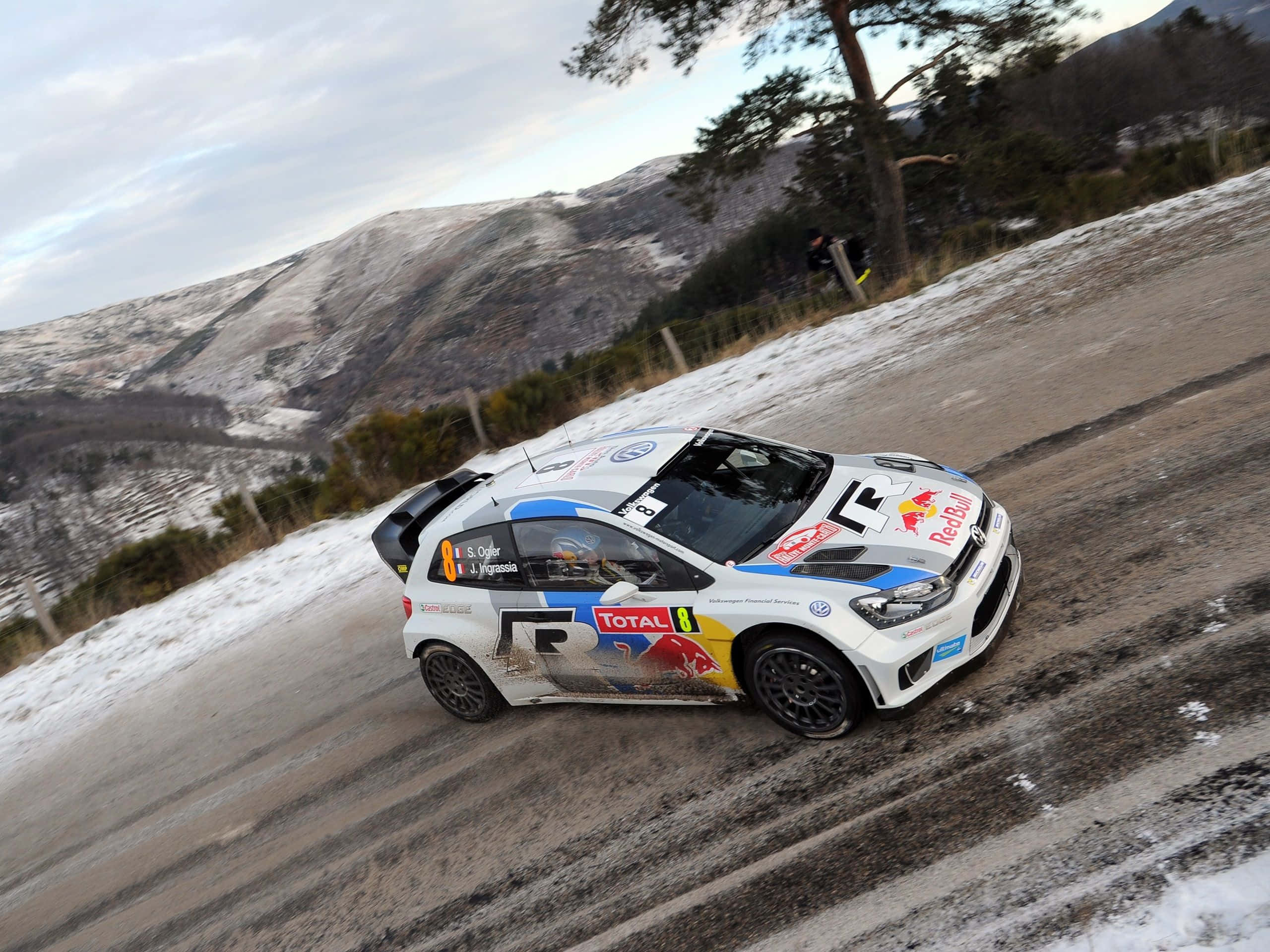 Ice Racing 桌布 壁紙 — 一輛帶有Red Bull和Total標誌的白色拉力賽車在雪山上疾馳，背景是松樹和積雪覆蓋的山丘。