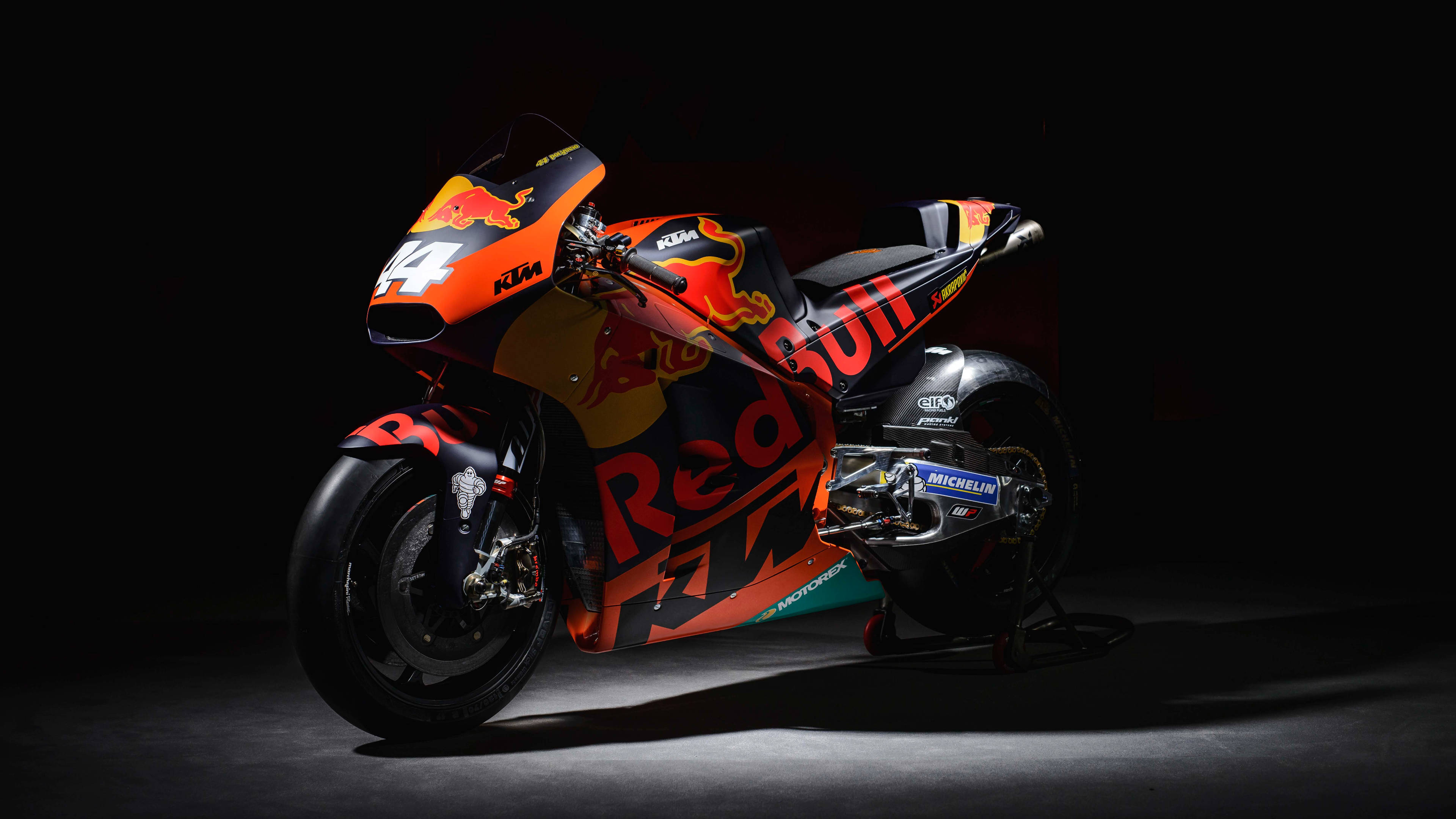 機車 桌布 壁紙 — 一輛帶有Red Bull品牌標誌的時尚KTM MotoGP機車，在黑色背景下於戲劇性的攝影棚燈光中閃耀。