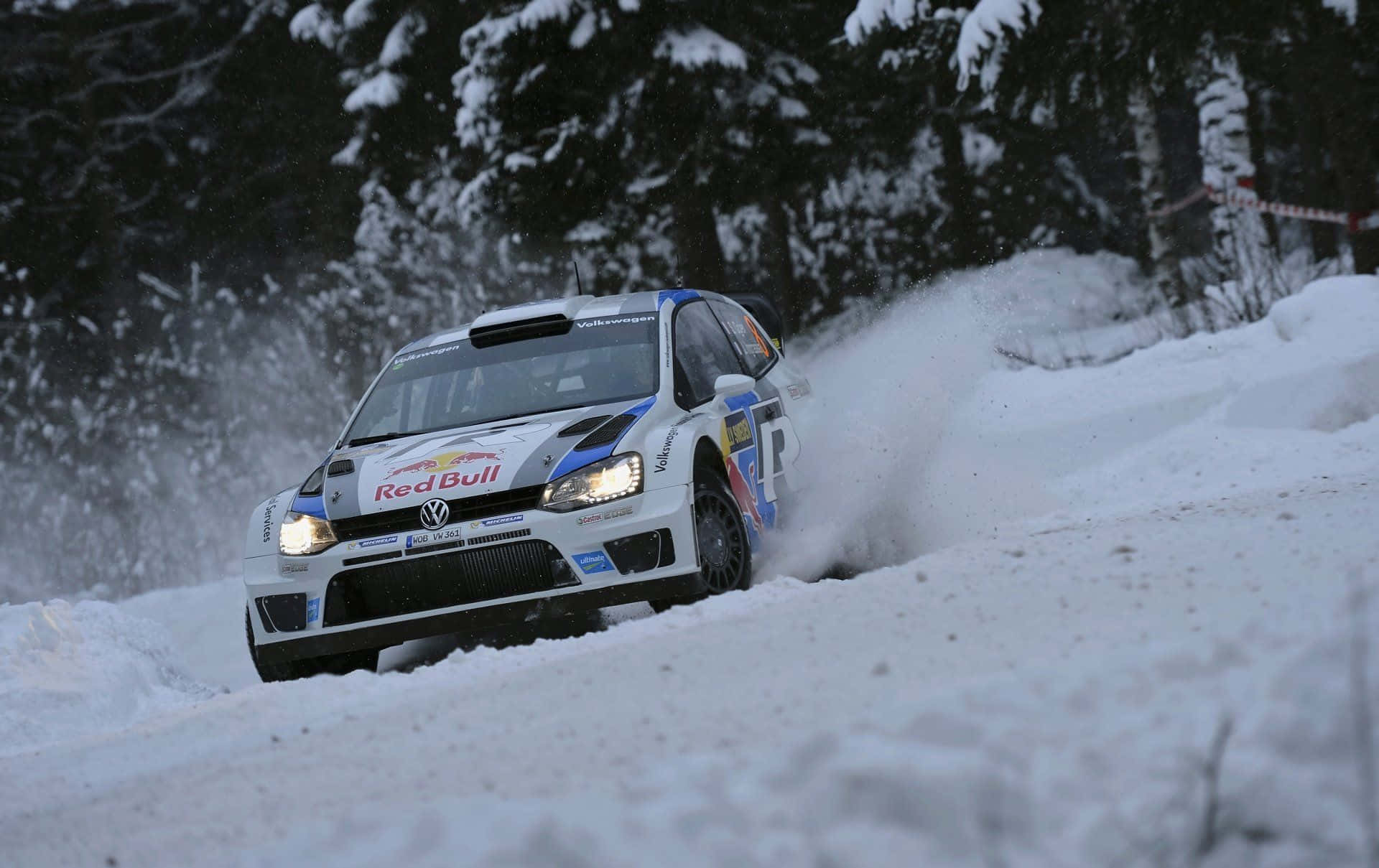 Ice Racing 桌布 壁紙 — 一輛帶有Red Bull標誌的白色福斯偉根拉力賽車在雪地森林賽道上飛馳，激起雪花。