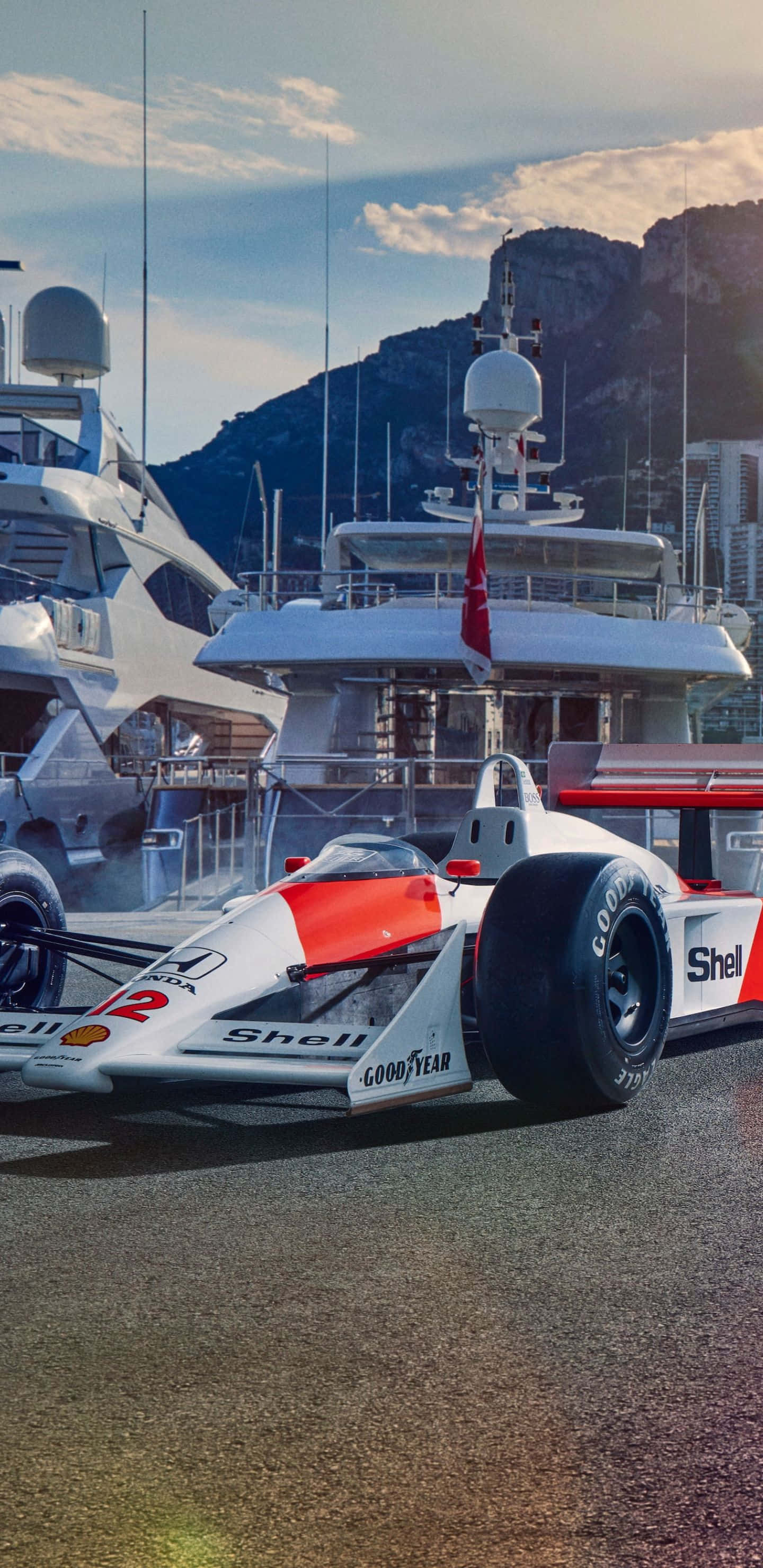 Formula 1 桌布 壁紙 — 一輛帶有Shell品牌標誌的白色和紅色復古一級方程式賽車停泊在碼頭 dock 上，旁邊是豪華遊艇，天空部分多雲。