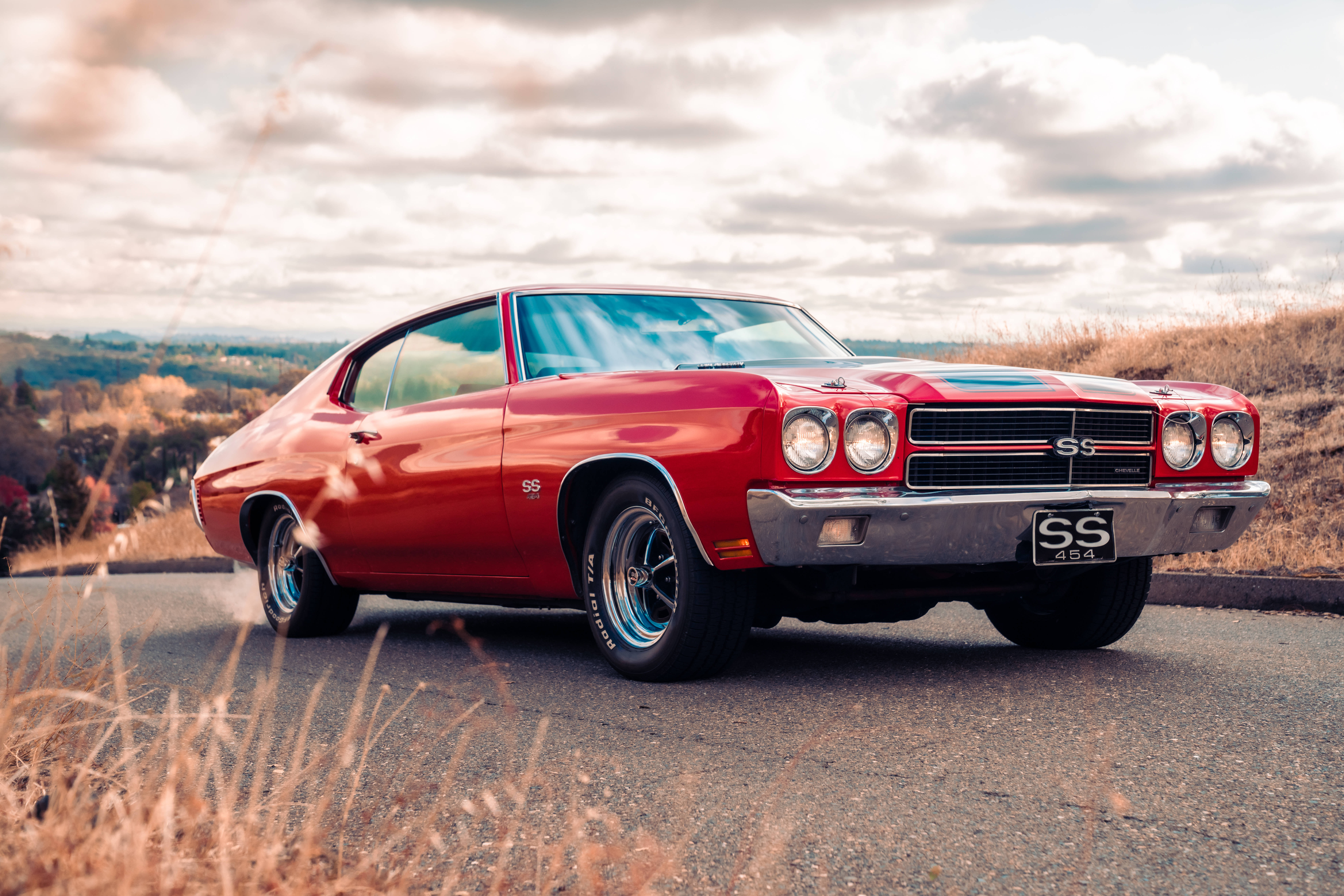 Chevrolet 桌布 壁紙 — 一輛帶有SS條紋的鮮紅色經典肌肉車停在蜿蜒的道路上，穿過金黃色的草地，天空多雲。