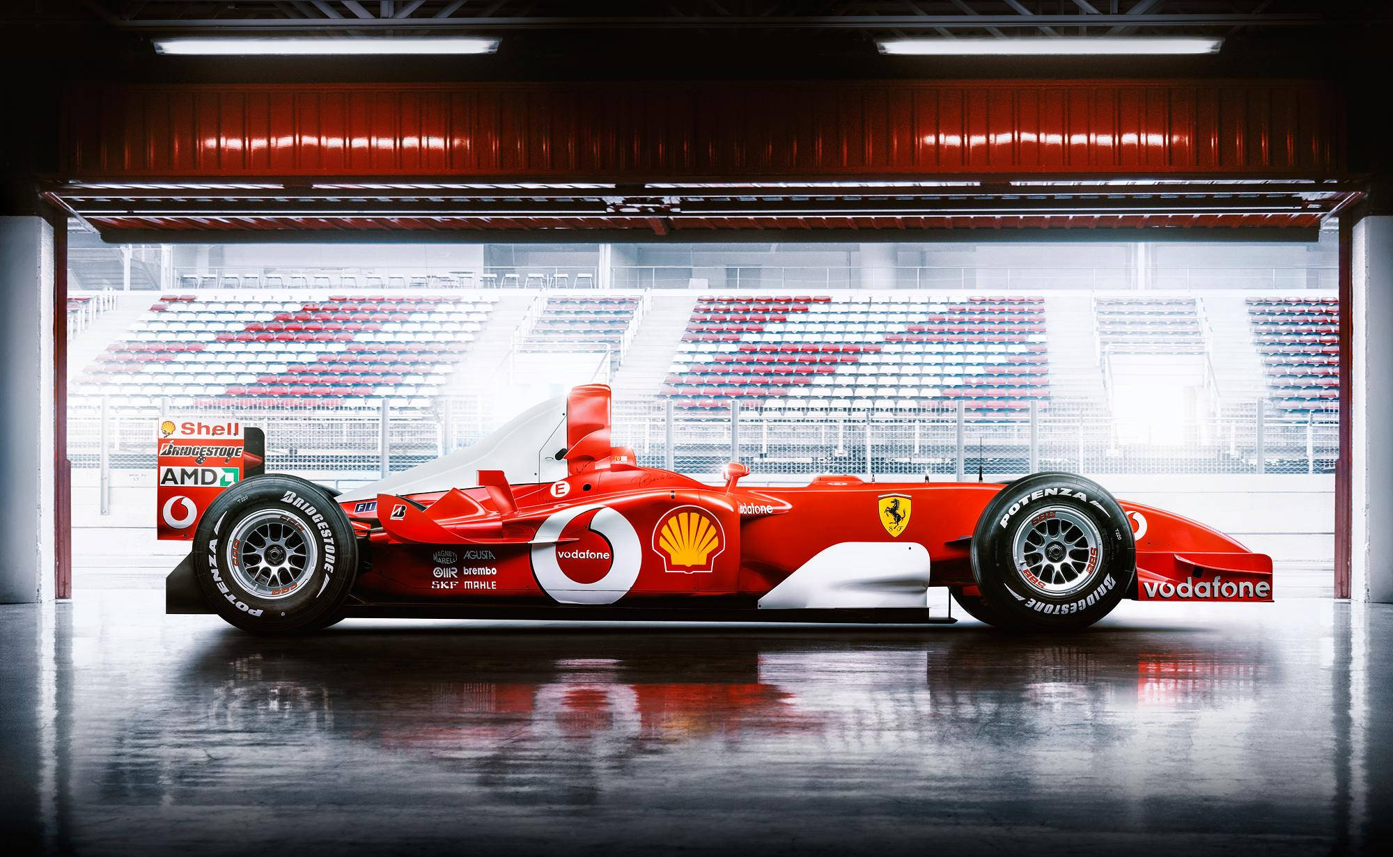 michael 桌布 壁紙 — 一輛帶有Vodafone和Shell標誌的鮮紅色法拉利F1賽車在潮濕的車庫中閃閃發光，後面可見空蕩蕩的看台。