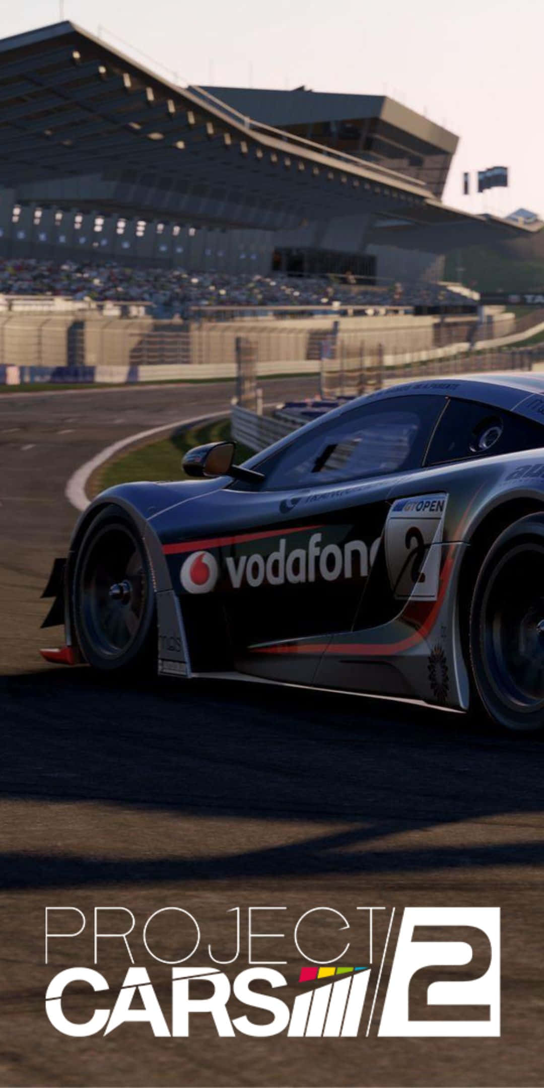 Pixel 3 Project Cars 2 桌布 壁紙 — 一輛帶有Vodafone標誌的時尚黑色賽車，在陽光普照的賽道上，於坐滿觀眾的看台下飛馳。