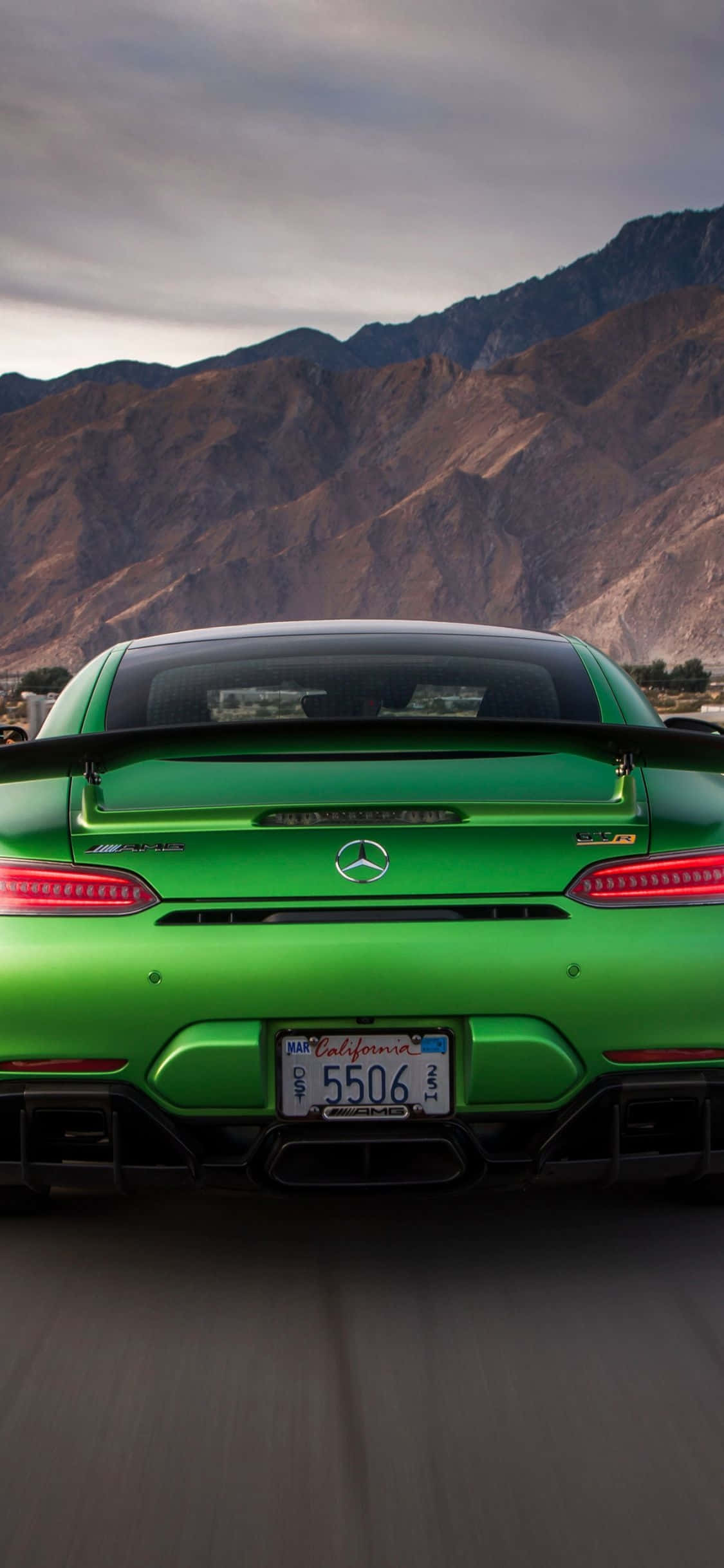 Mercedes 桌布 壁紙 — 一輛帶有加州車牌的鮮綠色 Mercedes-AMG GT R 跑車在陰天背景下，以崎嶇的棕色山脈為背景行駛在道路上。