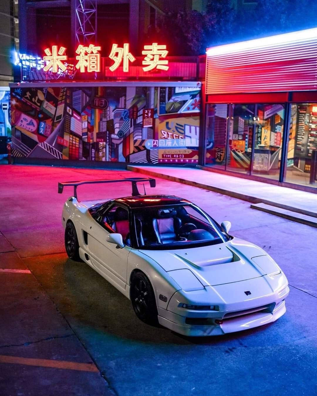 彩色動圖 桌布 壁紙 — 一輛帶有後擾流板的白色跑車在夜間停泊在霓虹燈照亮、紅色招牌閃爍的都市街道上。