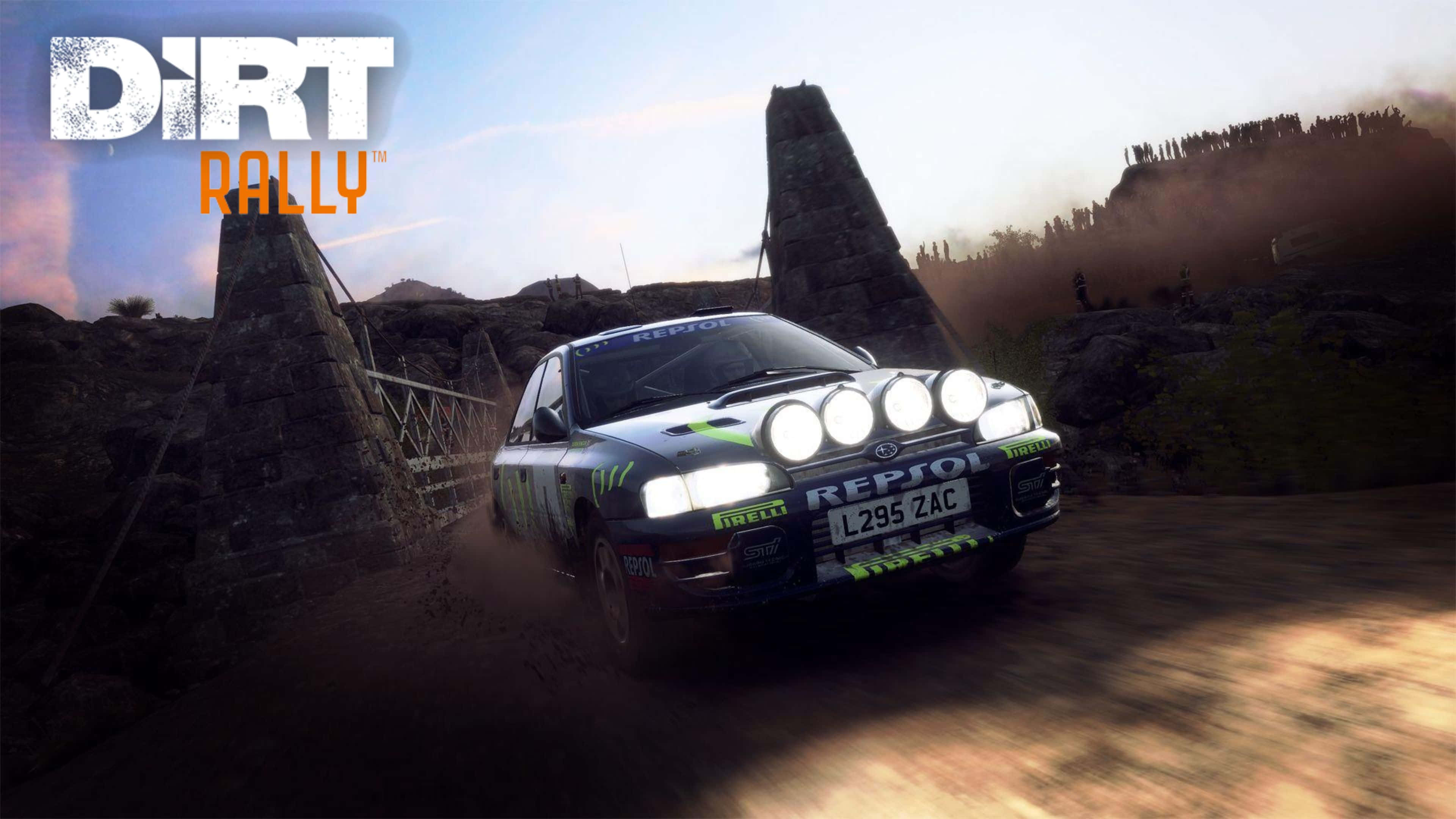 4K Dirt Rally 桌布 壁紙 — 一輛帶有明亮頭燈的拉力賽車在日落時分，於崎嶇的山地地形中疾速駛過一條塵土飛揚的石橋。