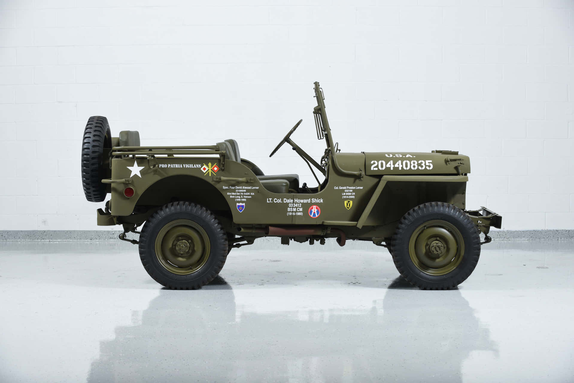 Jeep Willys 桌布 壁紙 — 一輛帶有星形徽章和部隊標誌的復古橄欖綠軍用吉普車，停在明亮白色且地板反光的工作室中。