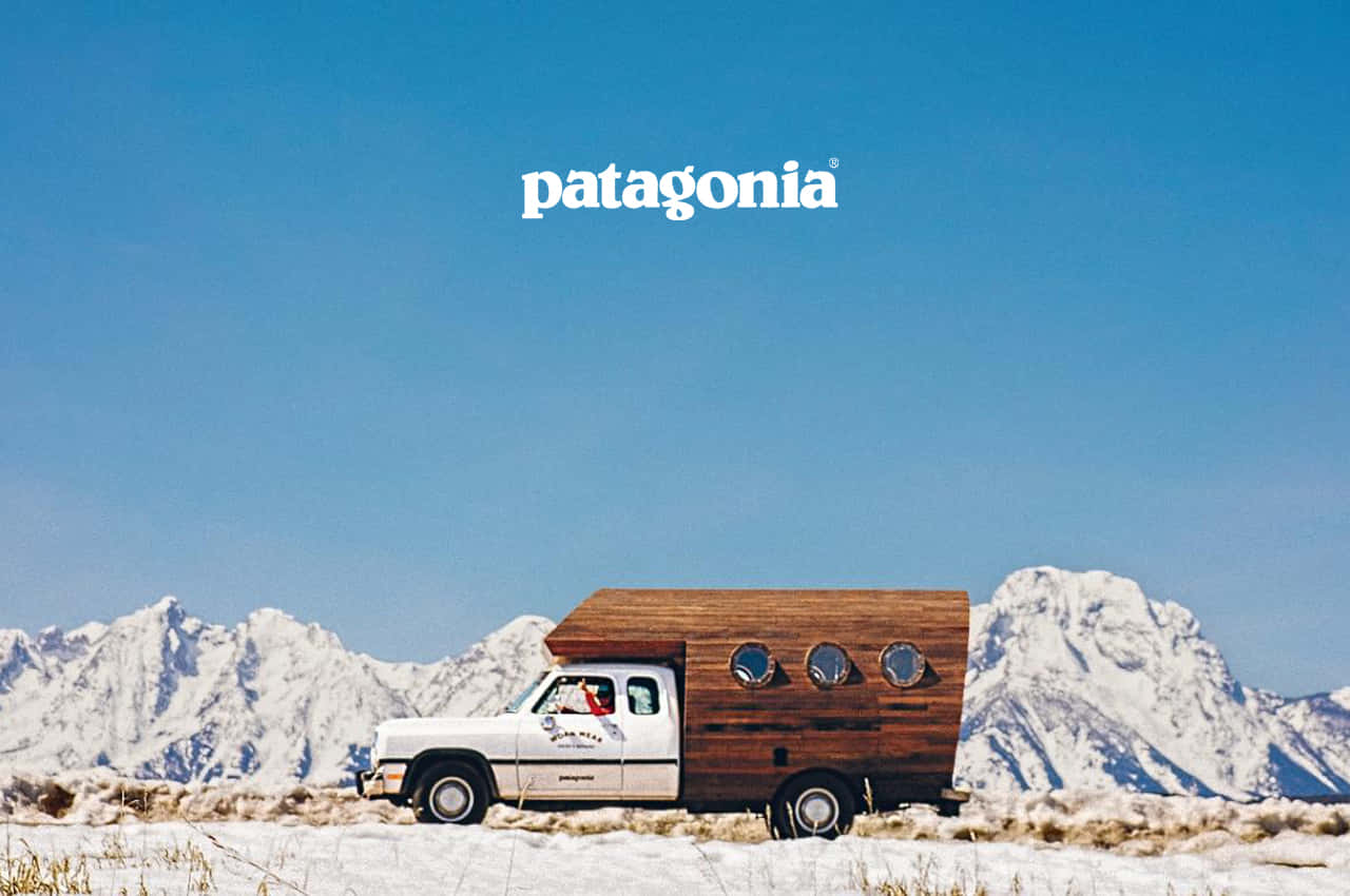 Patagonia 桌布 壁紙 — 一輛帶有木製露營車殼的白色卡車在雪地中行駛，背景是白雪覆蓋的山脈和清澈的藍天。