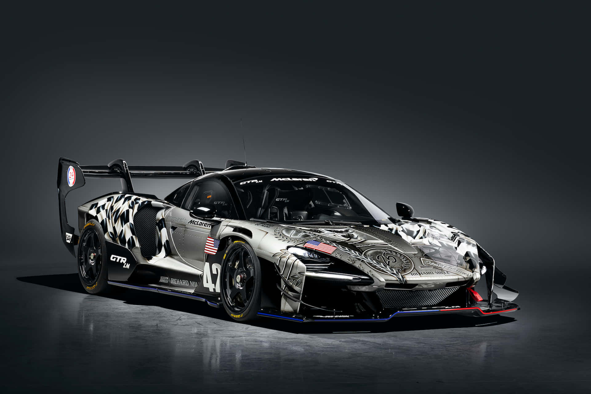 Mclaren Senna 桌布 壁紙 — 一輛帶有格子圖案和美國國旗的時尚銀黑色賽車，在戲劇性燈光下矗立在黑暗的攝影棚地板上。