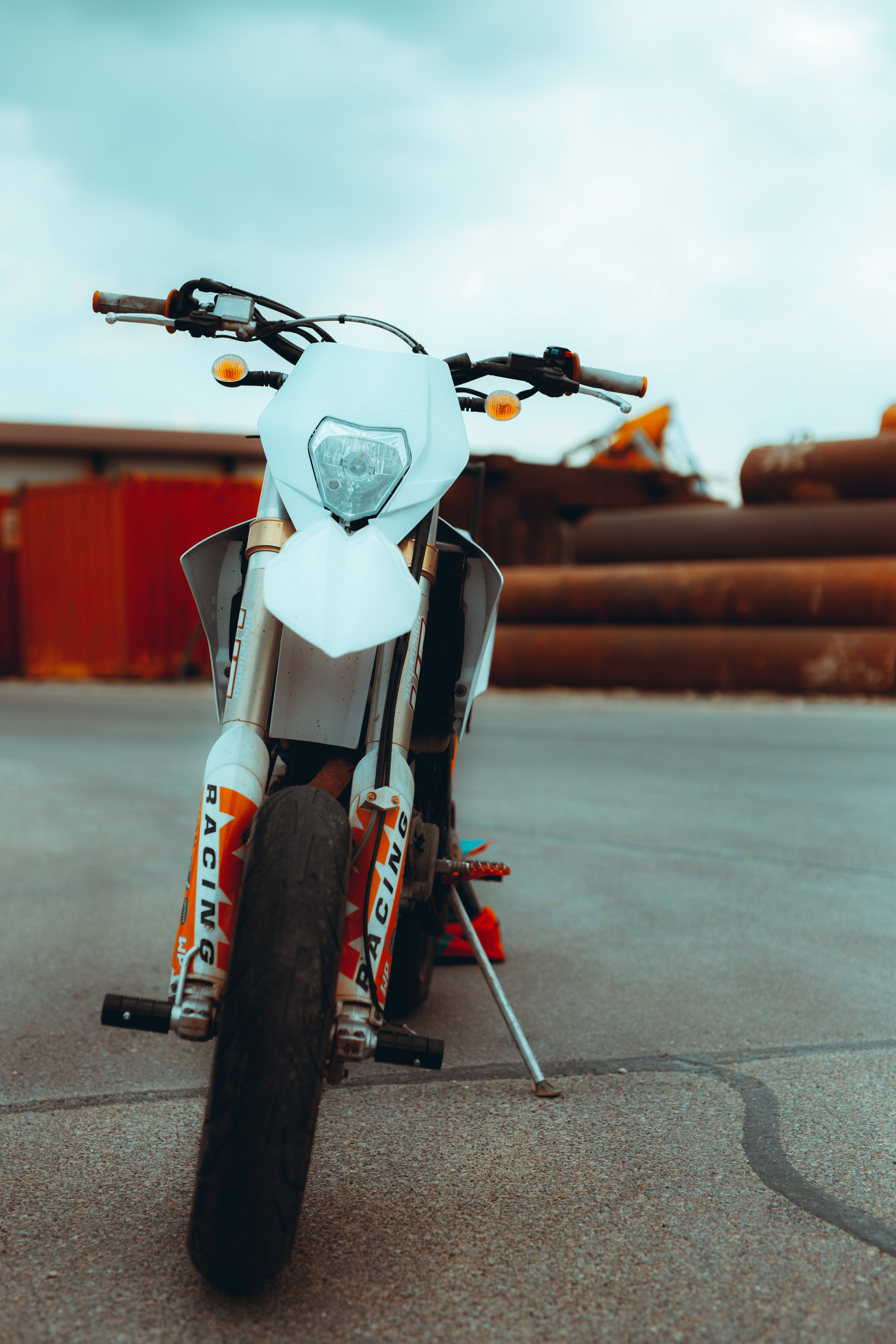 Ktm Bike 桌布 壁紙 — 一輛帶有橙色賽車貼紙的白色越野摩托車，在陰天底下用側腳架停放在混凝土場地上。