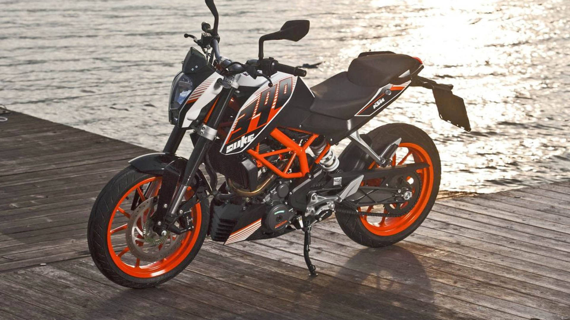  壁紙 — 一輛帶有橙色點綴的KTM Duke摩托車，在日落時停泊在波光粼粼的水邊木碼頭上。