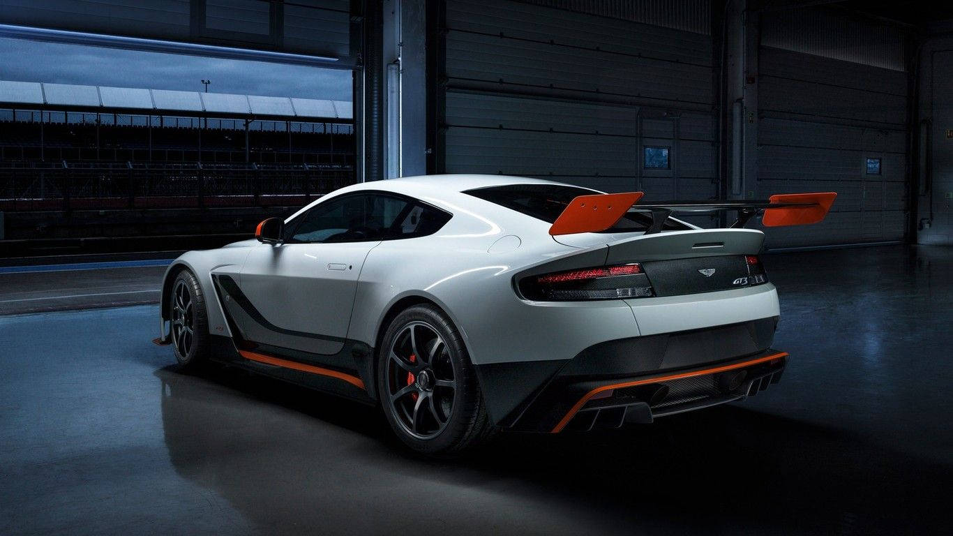 高清 桌布 壁紙 — 一輛帶有橙色點綴的時尚白色 Aston Martin Vantage GT12 在車庫燈光下閃閃發光，展現其空氣動力學設計和大型尾翼。