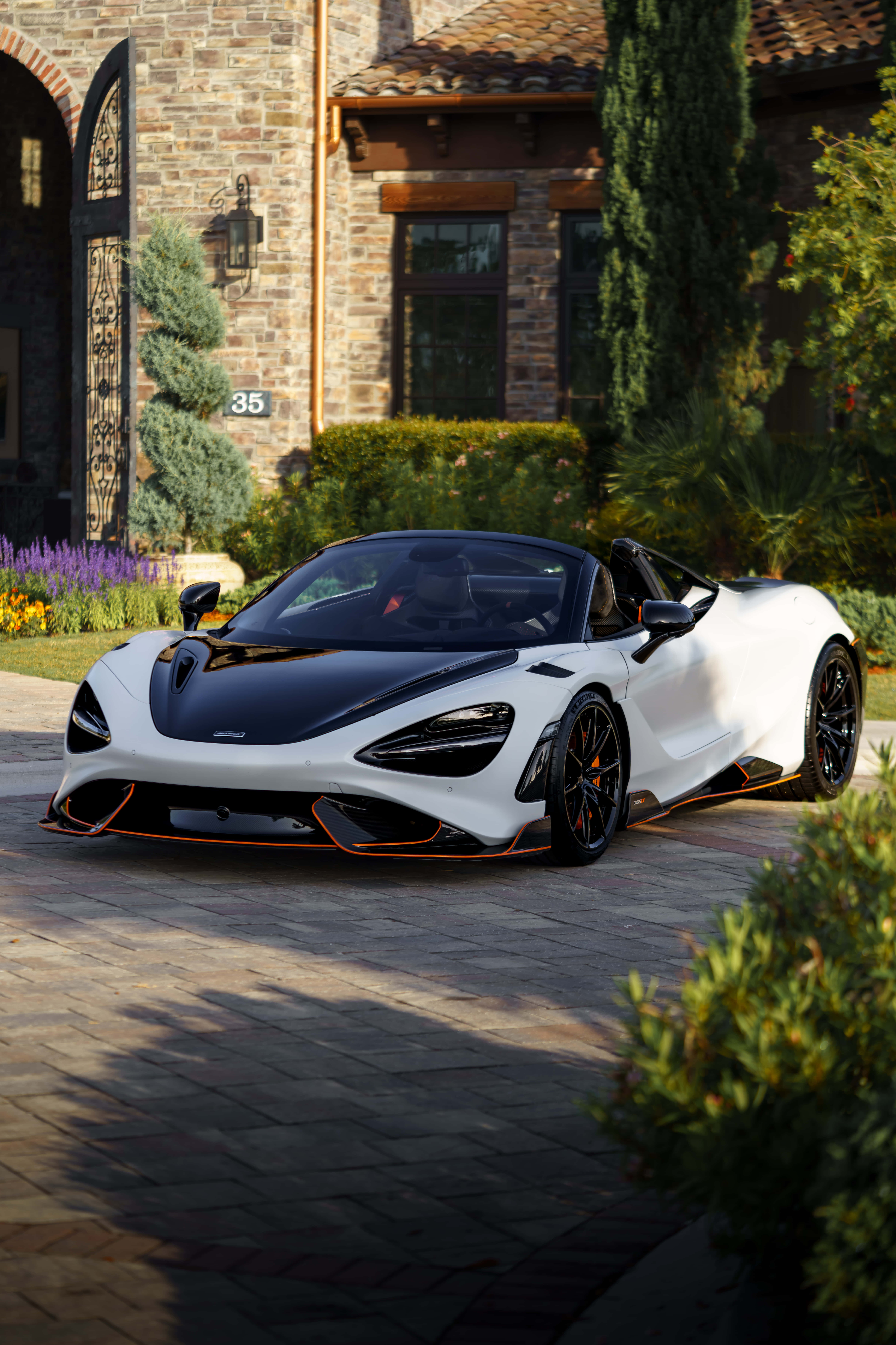 麥拉倫 桌布 壁紙 — 一輛帶有橙色點綴的白色和黑色McLaren Speedtail敞篷車停在豪華石砌豪宅前的石頭車道上。