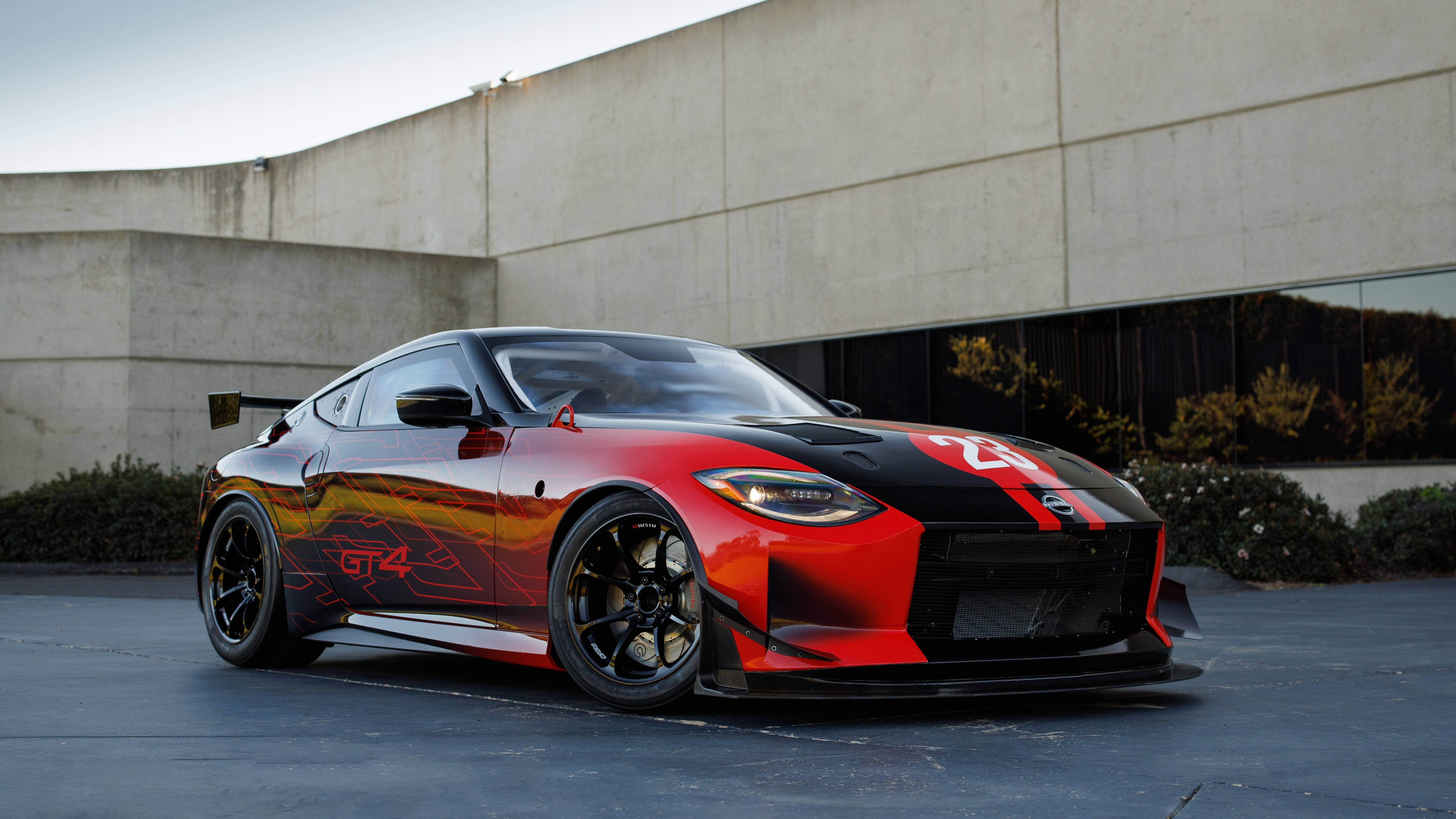 日產 桌布 壁紙 — 一輛帶有火焰貼紙的紅黑色日產GT4賽車停在一棟現代混凝土建築前。