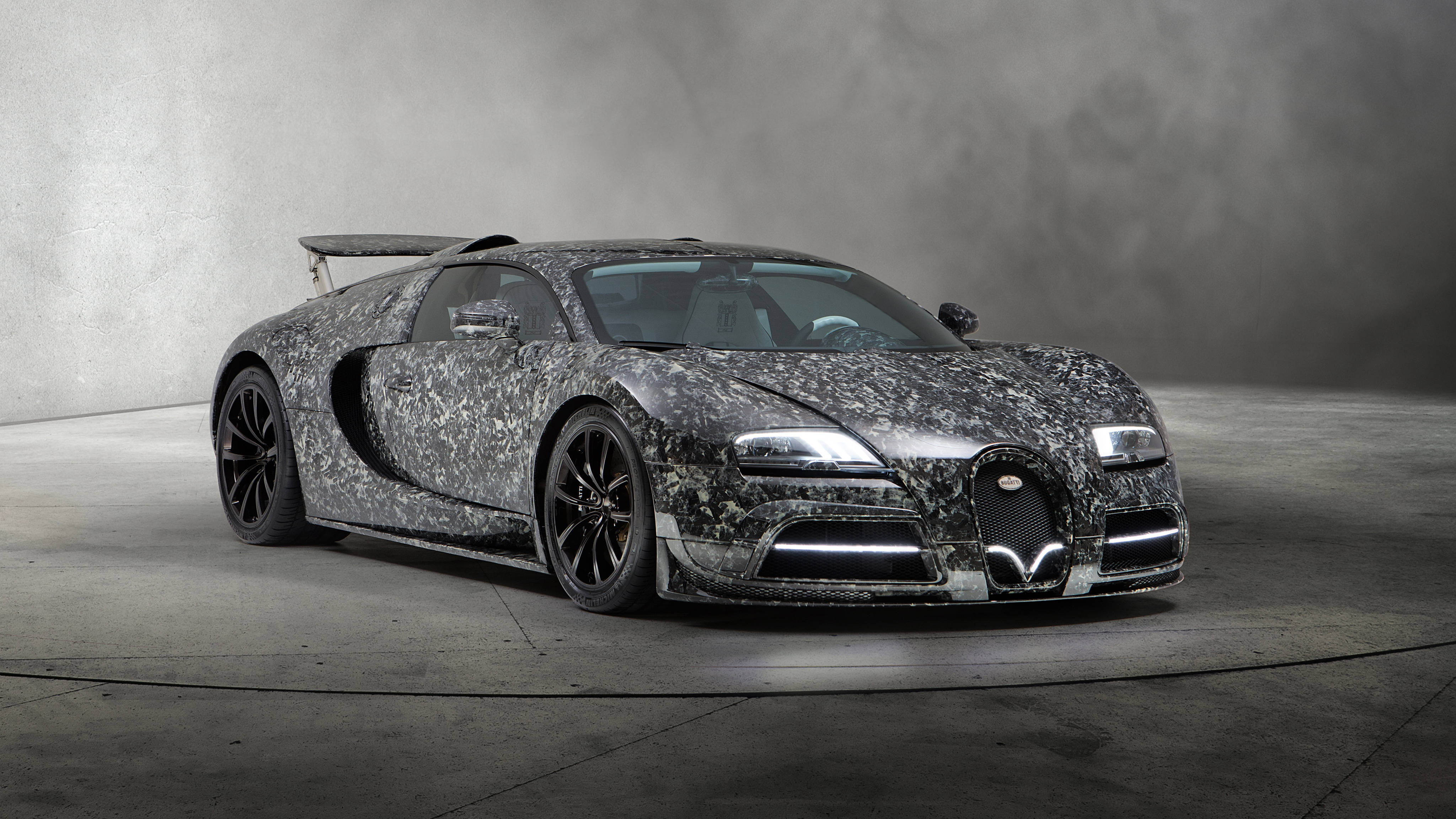 Cool Bugatti 桌布 壁紙 — 一輛帶有灰色和黑色斑點迷彩圖案的Bugatti超級跑車，在極簡混凝土工作室的戲劇性燈光下蓄勢待發。