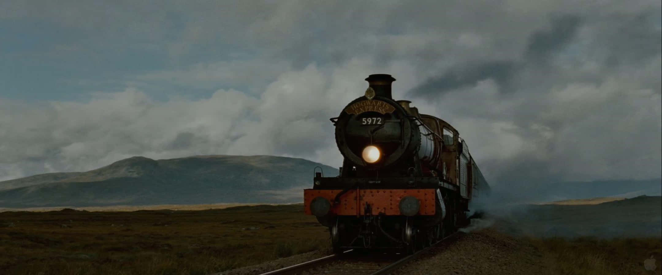 The Hogwarts Express Train 桌布 壁紙 — 一輛帶有發光頭燈的復古蒸汽火車，在陰雲密佈、氣氛憂鬱的蘇格蘭高地景觀中緩緩行駛。