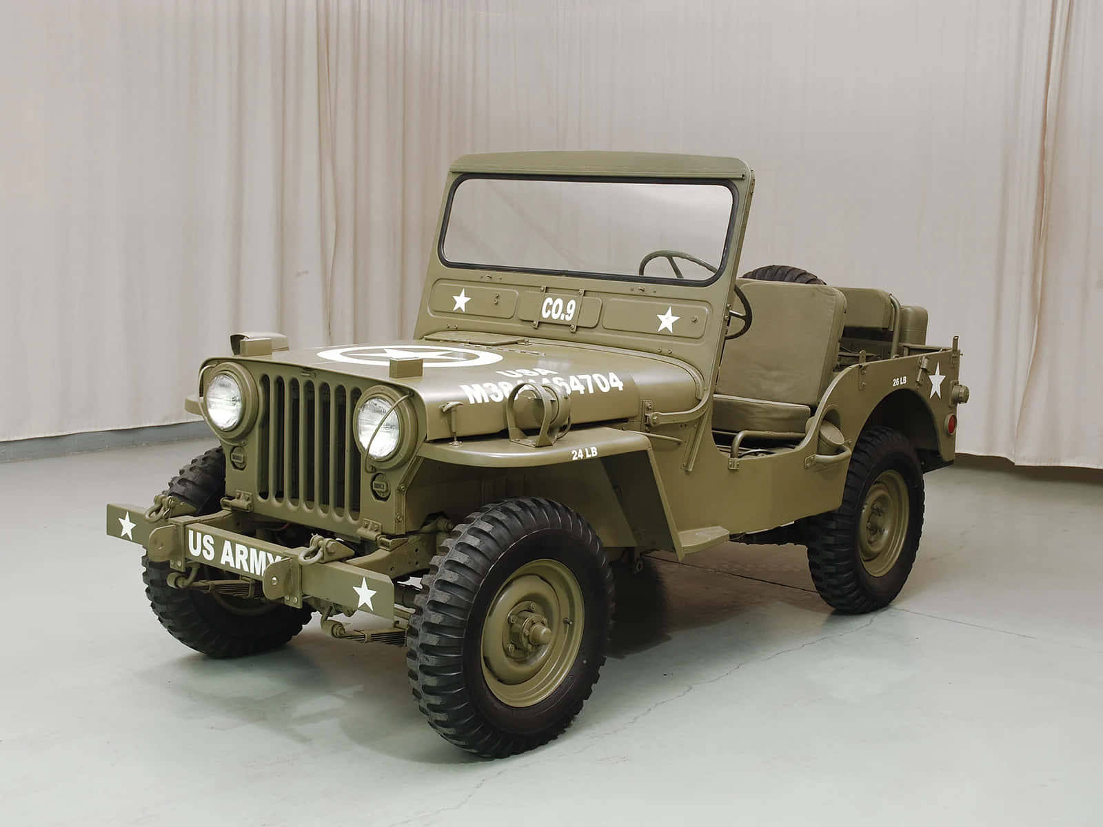 Jeep Willys 桌布 壁紙 — 一輛帶有白色星星和標記的復古橄欖色美國陸軍吉普車停在乾淨的室內空間。