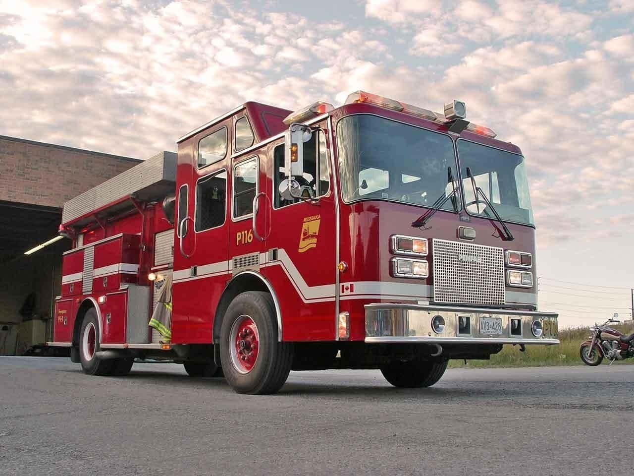 Fire Truck 桌布 壁紙 — 一輛帶有白色條紋的光亮紅色消防車停在磚砌消防局外，黃昏時分天空多雲。