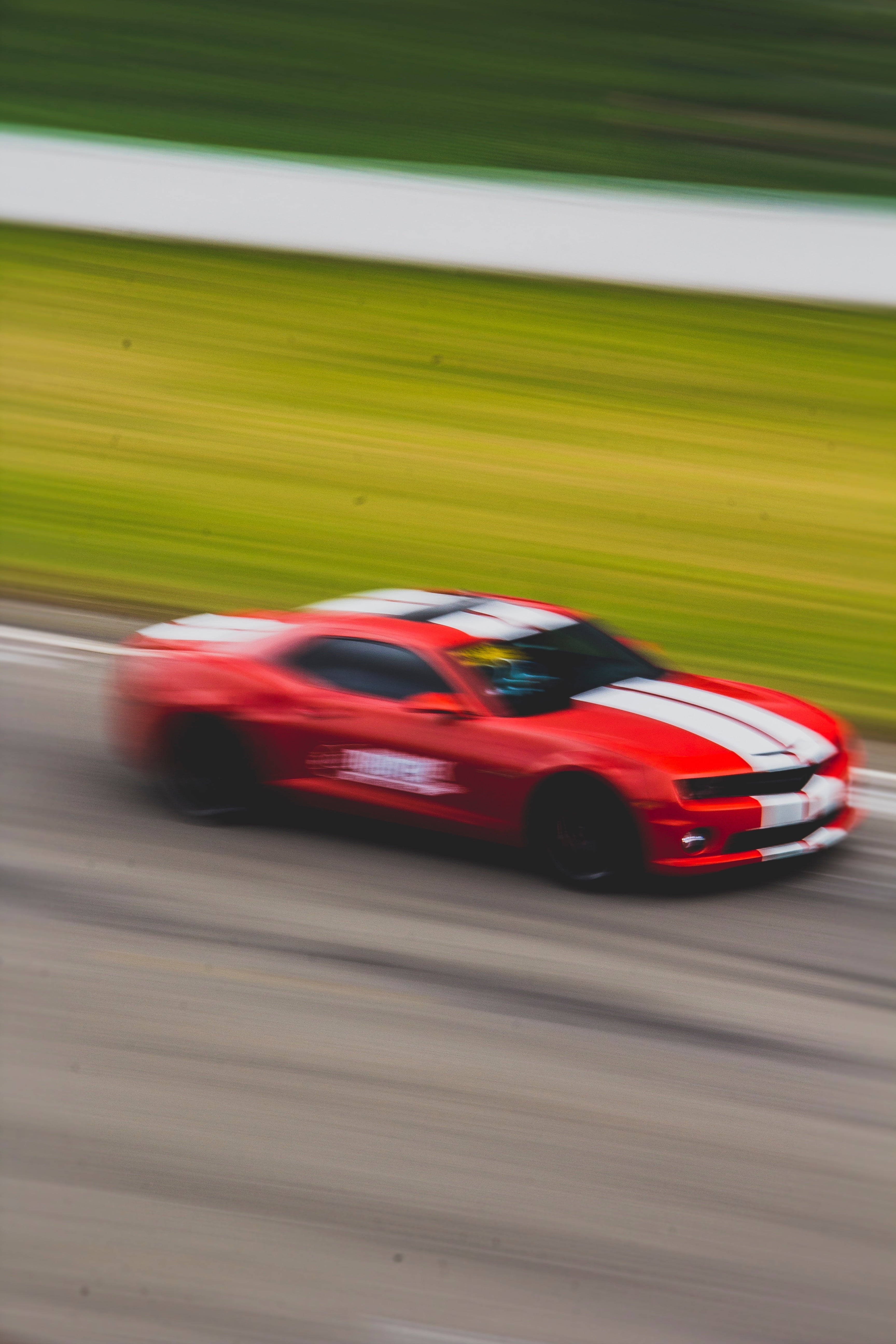 speeding car 桌布 壁紙 — 一輛帶有白色條紋的紅色賽車在賽道上飛馳，背景是帶條紋的綠色草地和白色護欄。