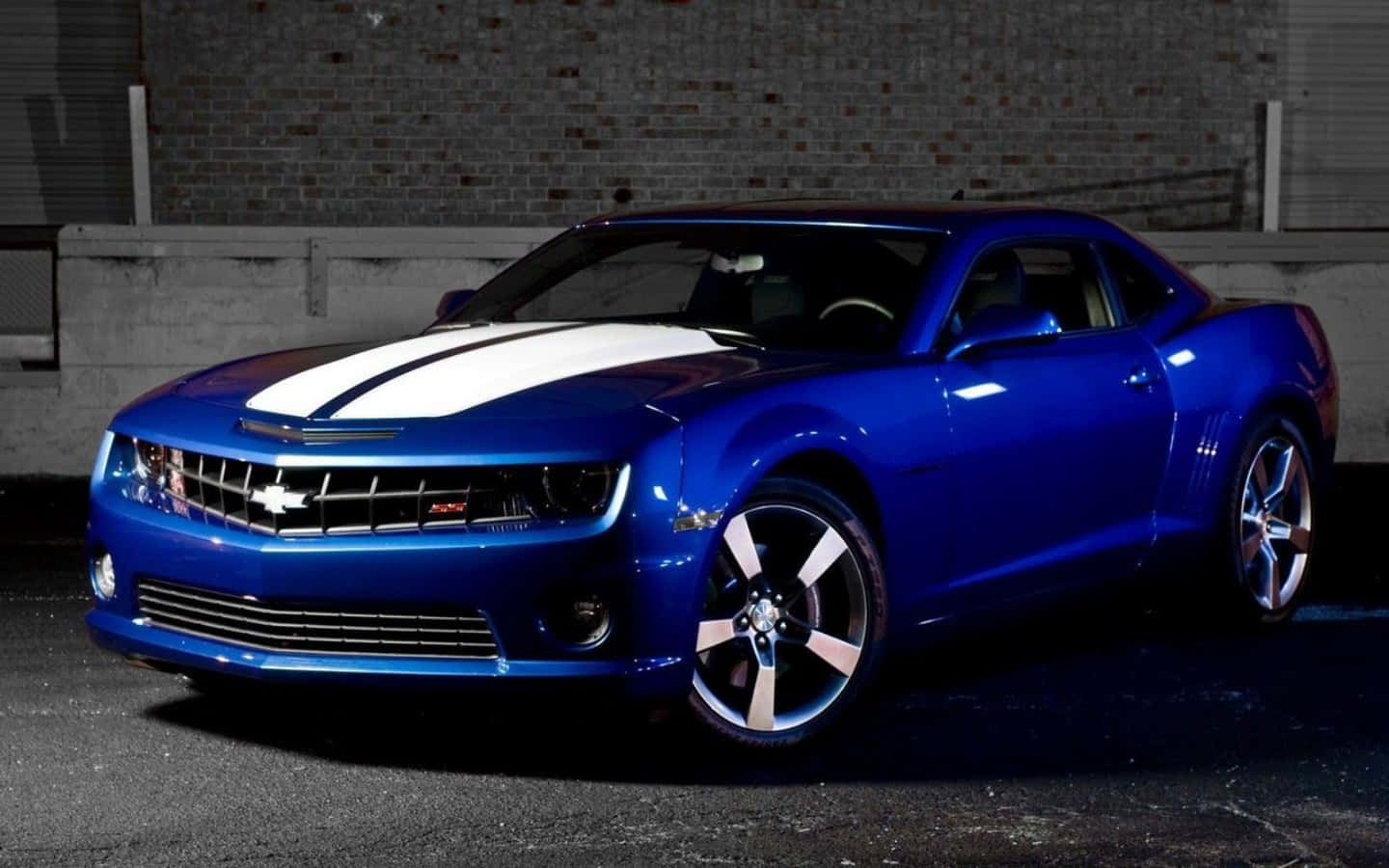 Chevrolet 桌布 壁紙 — 一輛帶有白色賽車條紋的亮藍色雪佛蘭 Camaro SS 在夜間停靠在磚牆旁。