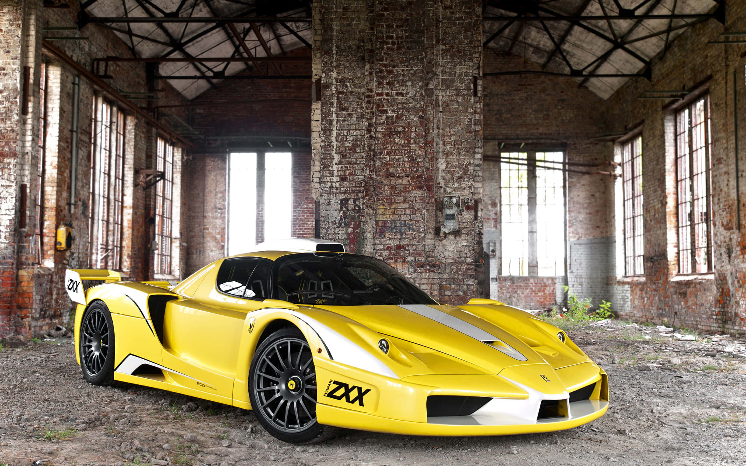 Ferrari Enzo 桌布 壁紙 — 一輛帶有白色賽車條紋的亮黃色法拉利Enzo停放在一個有高窗的風化磚倉庫內。