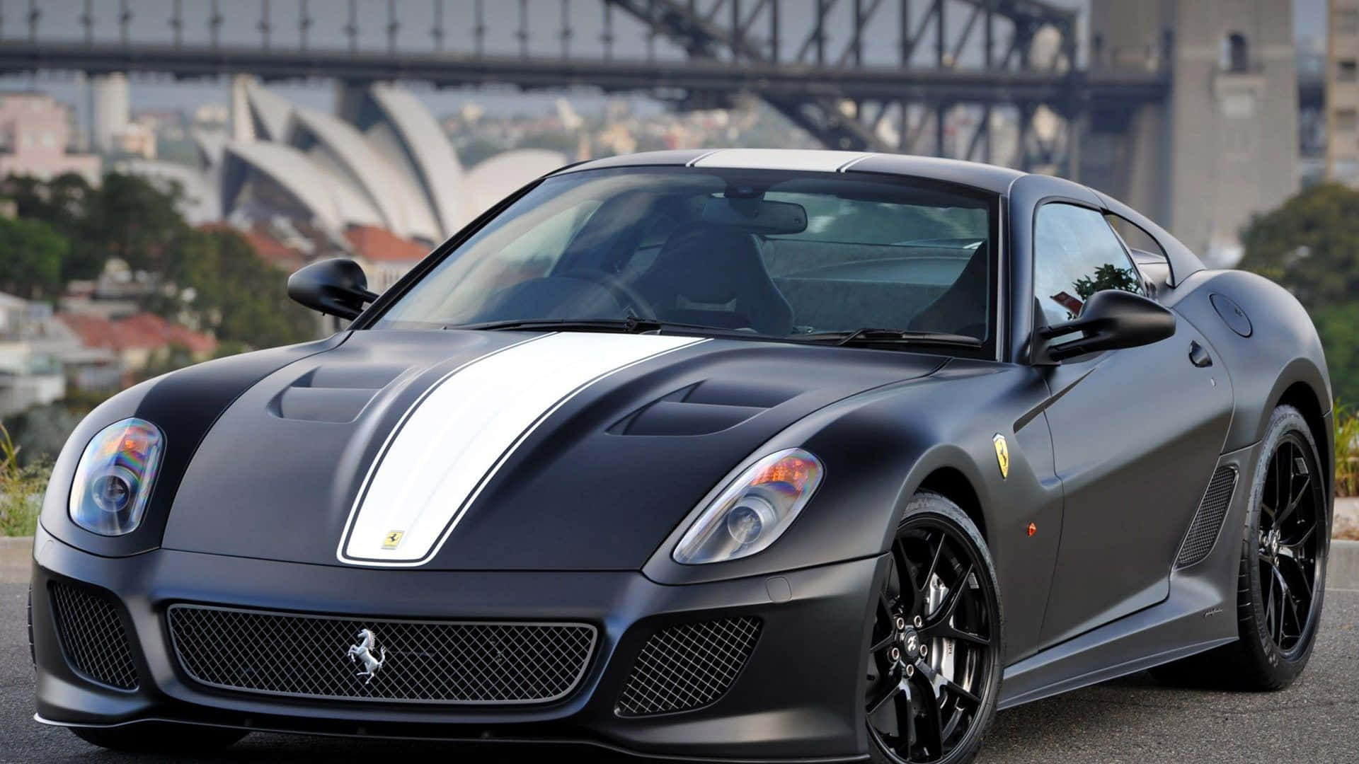 Ferrari 599 Gtb Fiorano 桌布 壁紙 — 一輛帶有白色賽車條紋的消光黑色法拉利跑車停放在雪梨歌劇院和港灣大橋前。