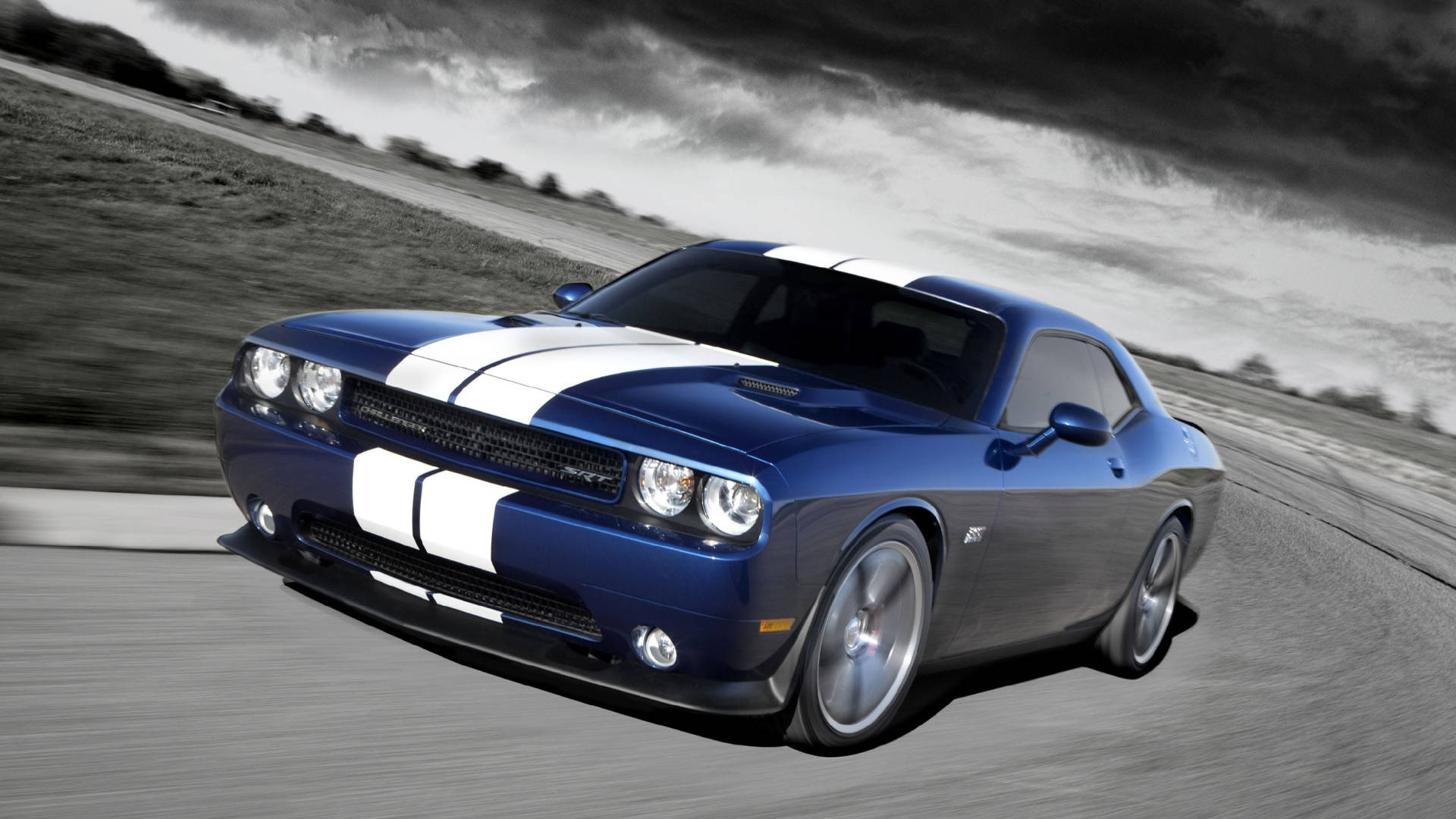 道奇挑戰者 桌布 壁紙 — 一輛帶有白色賽車條紋的藍色 Dodge Challenger 在暴風雨的天空下沿著模糊的瀝青道路飛馳。