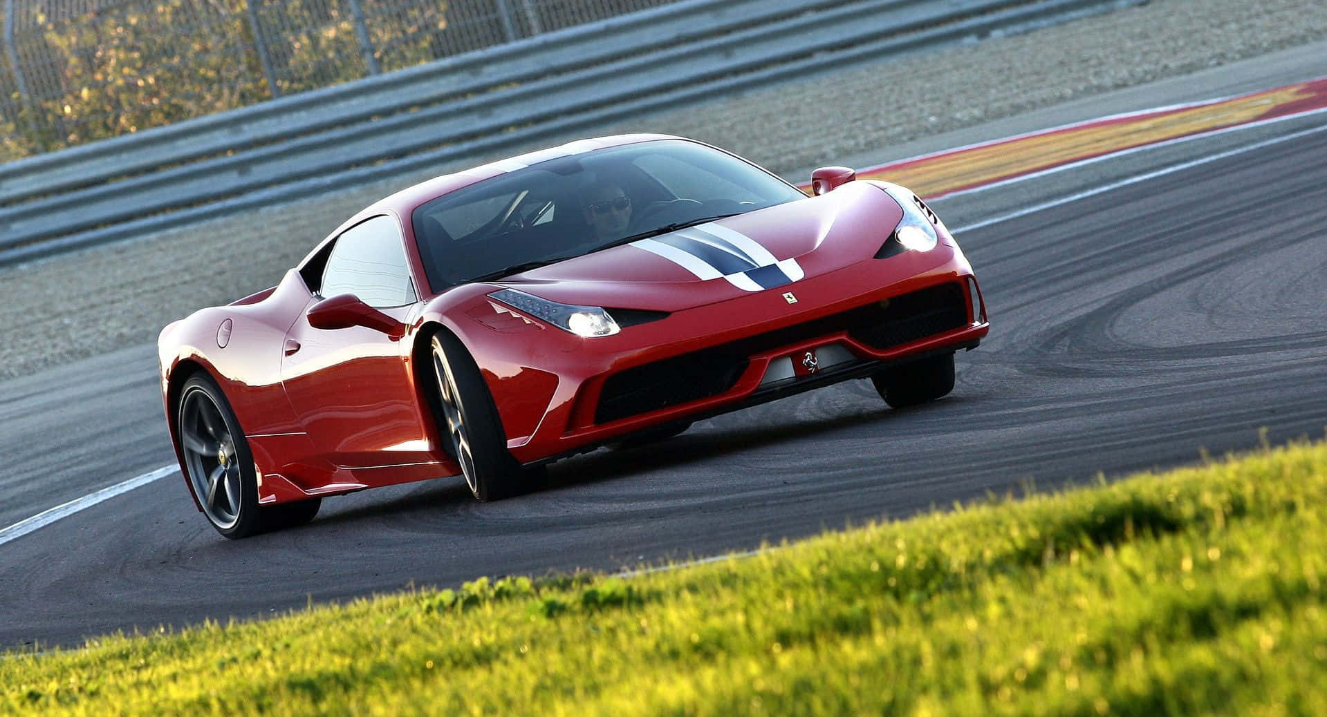 Ferrari 458 Speciale 桌布 壁紙 — 一輛帶有白色賽車條紋的鮮紅色法拉利跑車在賽道彎道上疾馳，前景是綠色草地。