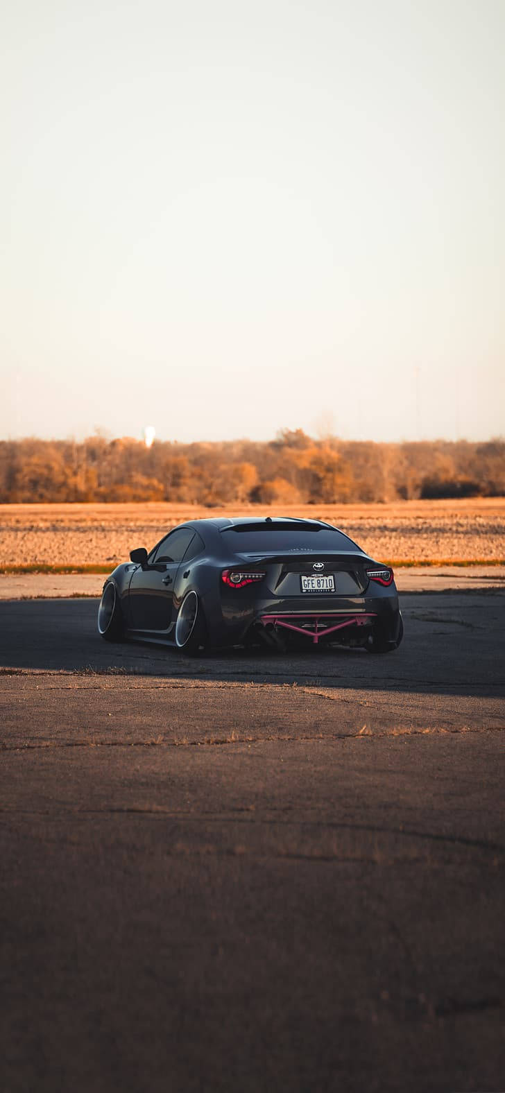 Auto Racing 桌布 壁紙 — 一輛帶有粉紅色點綴的時尚黑色跑車停在柏油路上，正值黃金時刻，周圍是秋日的田野和樹木。
