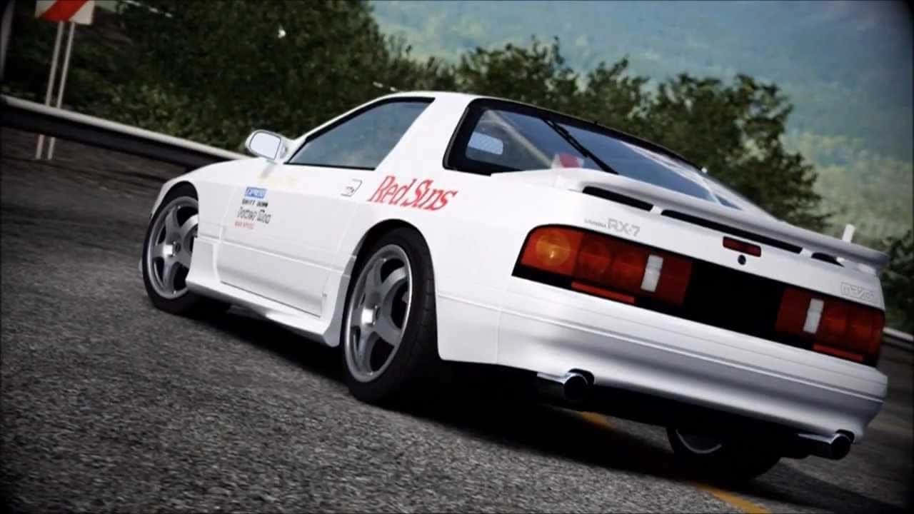 Rx7 Fc 桌布 壁紙 — 一輛帶有紅色「Red Suns」貼紙的白色日產RX-7跑車，在綠樹環繞的蜿蜒瀝青路上疾馳。