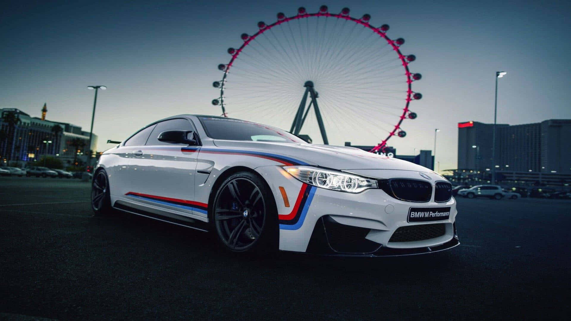 1920x1080 M Series 桌布 壁紙 — 一輛帶有紅色、藍色和橙色賽車條紋的白色BMW M4雙門跑車在黃昏時停放在倫敦眼前面。